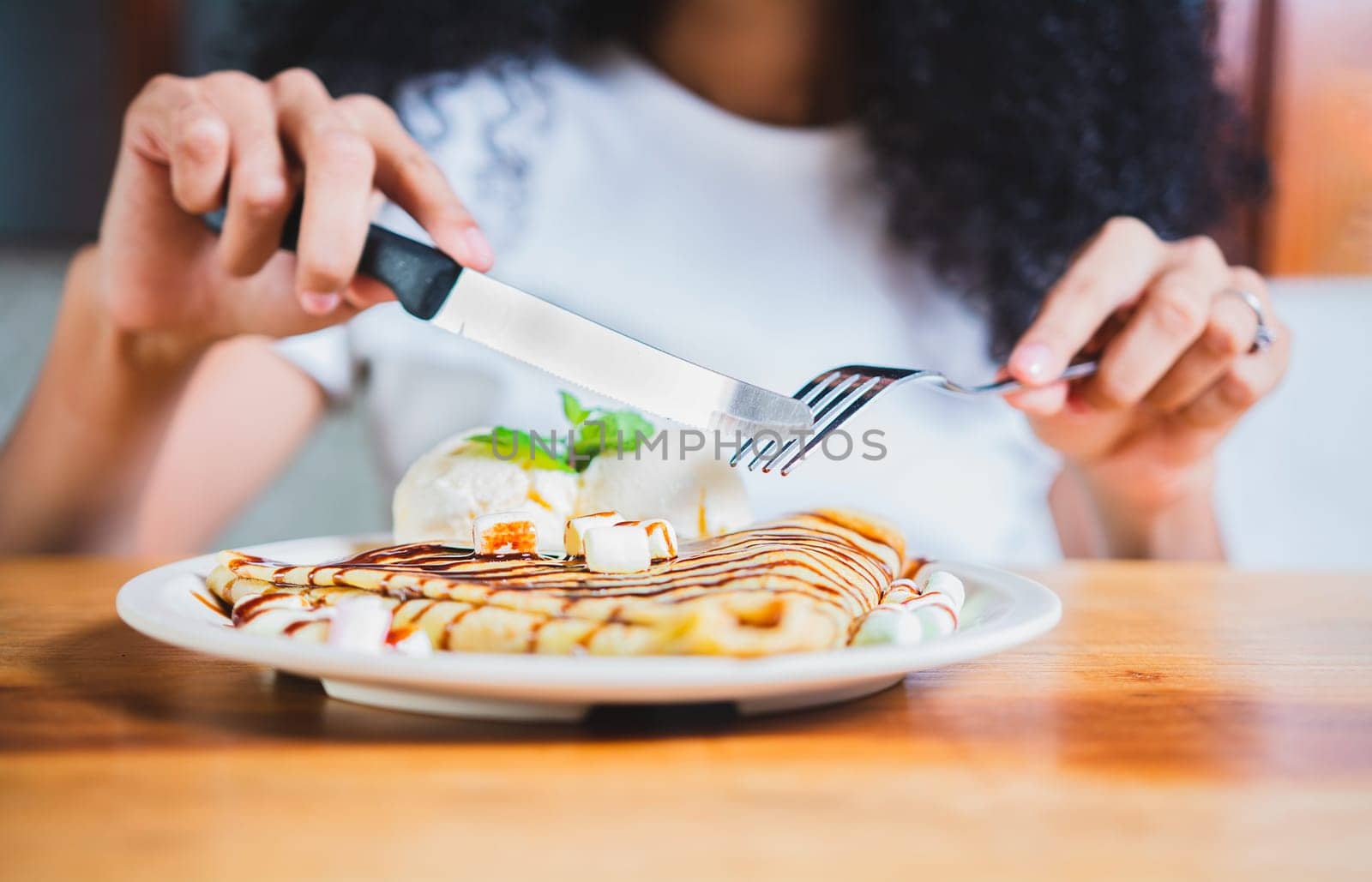 Woman hands eating chocolate crepe and ice cream with fork. Close up of woman eating a chocolate crepe with fork