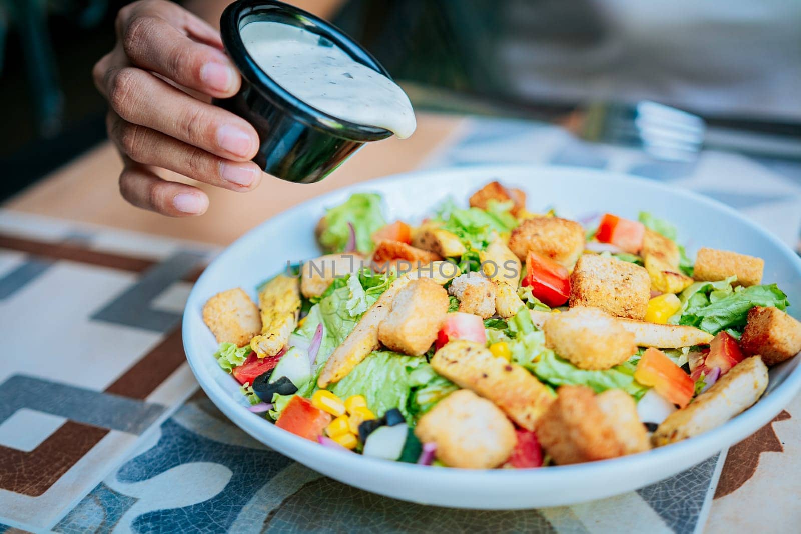 Hand putting dressing on a caesar salad. Close up of hand preparing a vegetable salad. Concept of healthy food and lifestyle by isaiphoto