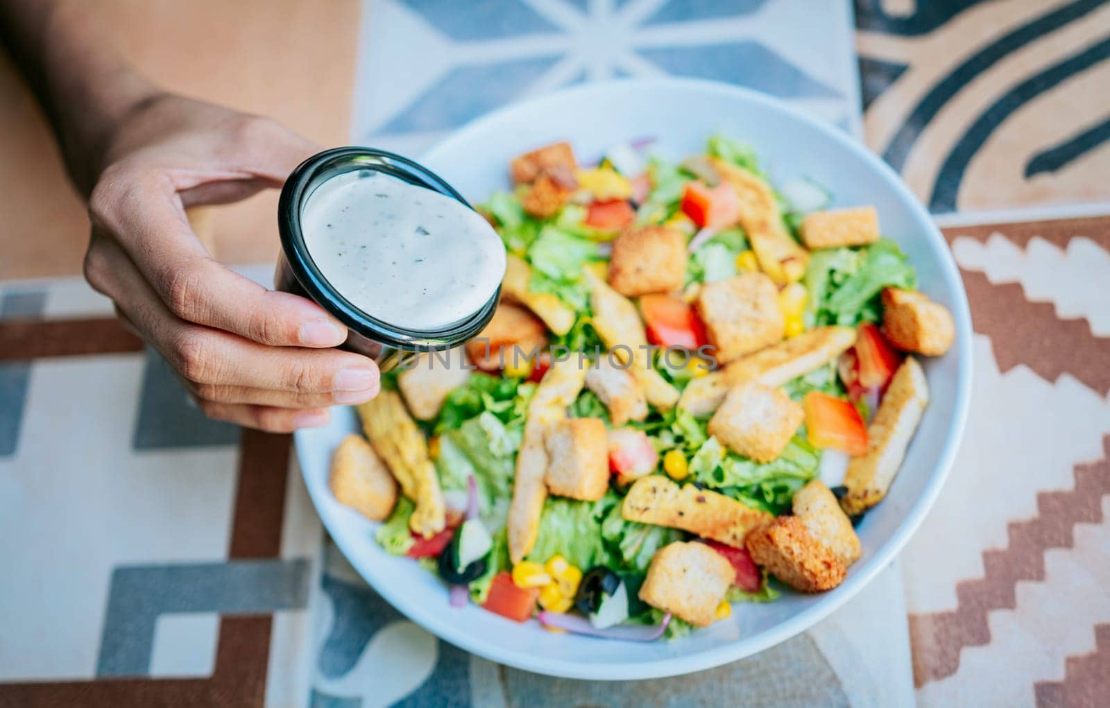 Concept of healthy food and lifestyle. Hand putting dressing on a caesar salad, Close up of hand preparing a vegetable salad by isaiphoto