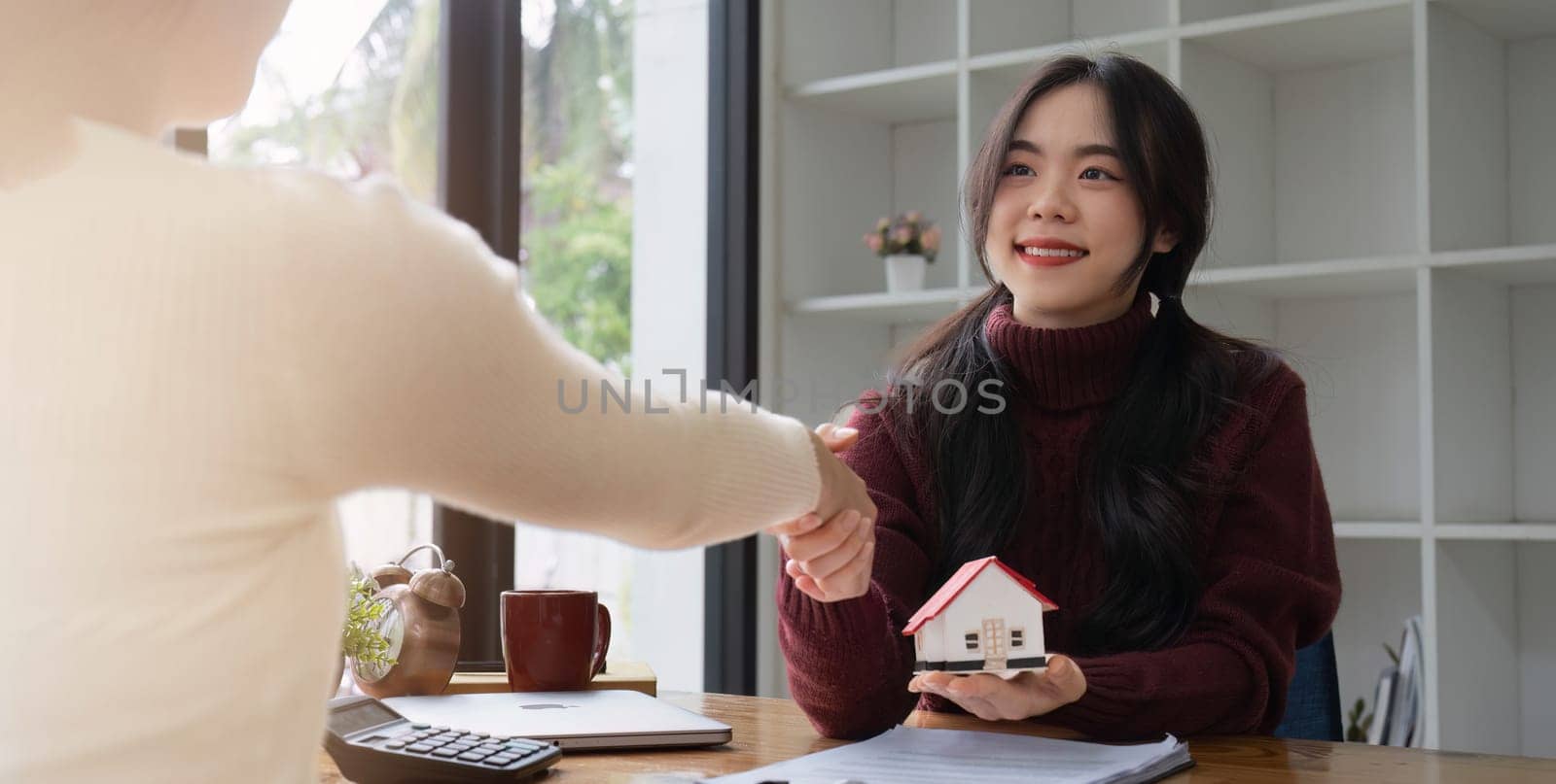 Real estate agents and customers shake hands to congratulate on signing a contract to buy a house with land.