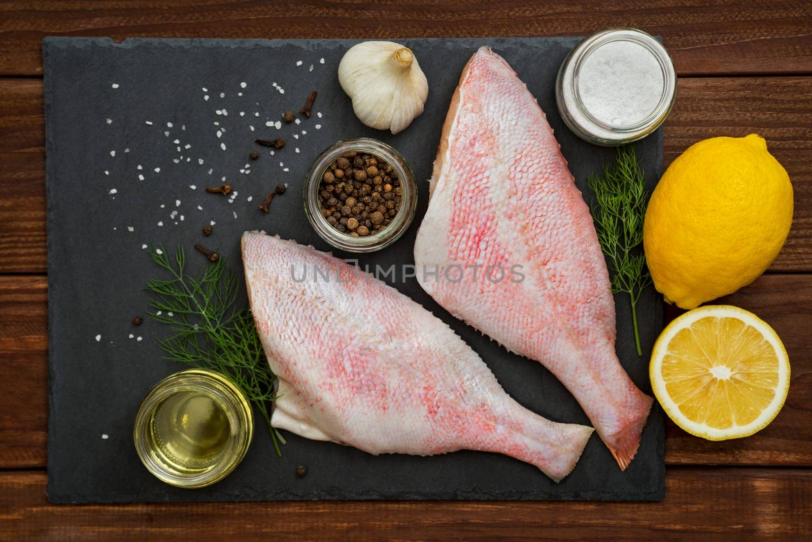 Seafood. Sea perch on a black board. Red sea bass on a black board with the ingredients for it cooking. Fish on the table. Ocean perch.