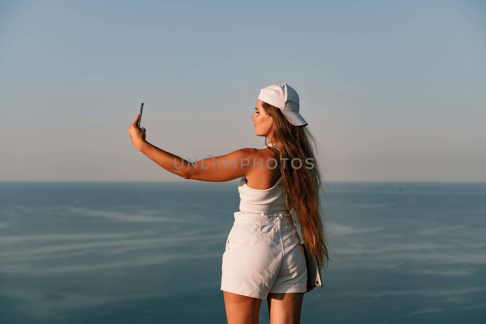 Selfie woman in a cap, white tank top and shorts makes a selfie shot mobile phone post photo social network outdoors on the background of the sea beach people vacation lifestyle travel concept