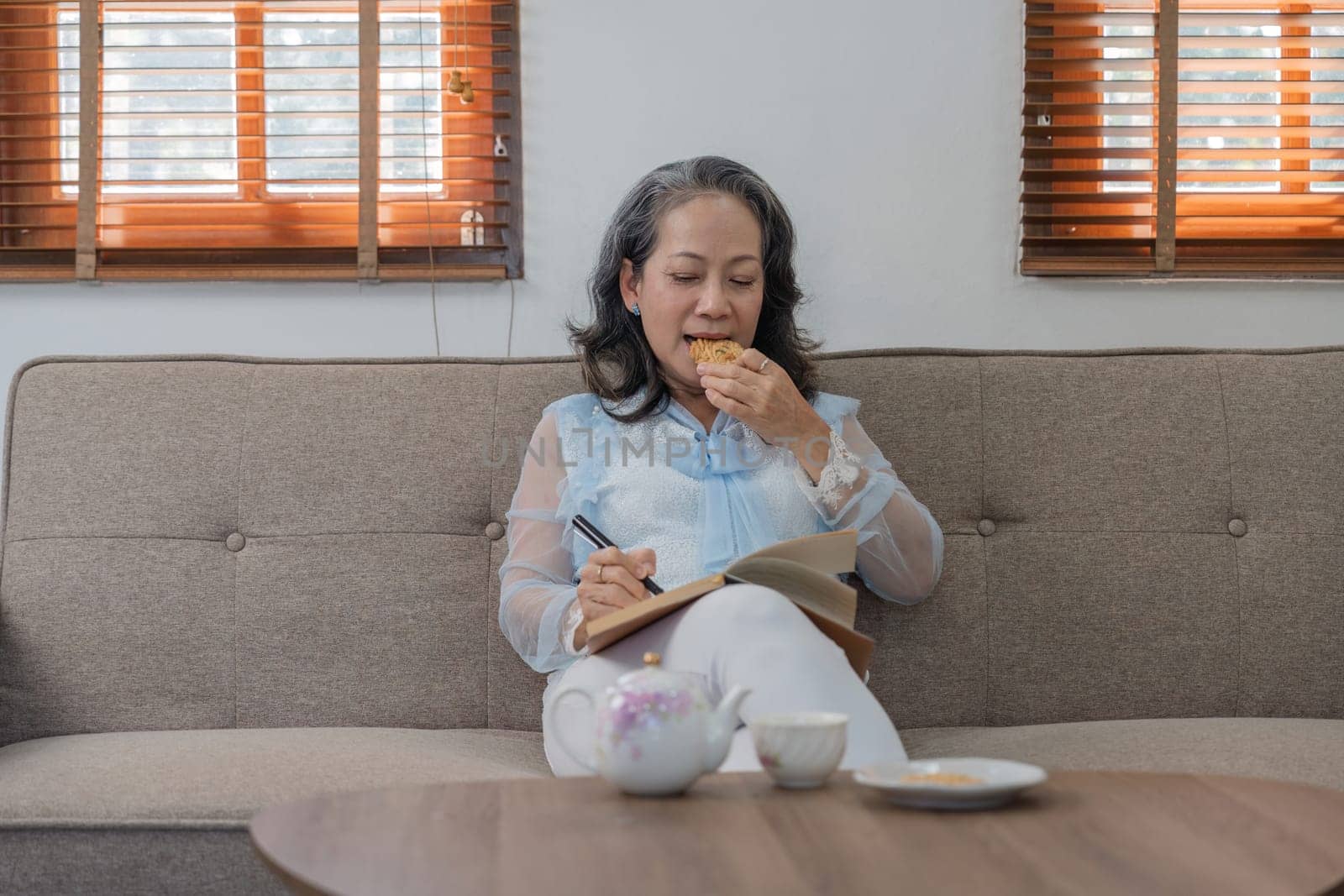 Happy Asian retired woman enjoying reading Books and notes on the subject of health care in home relaxed