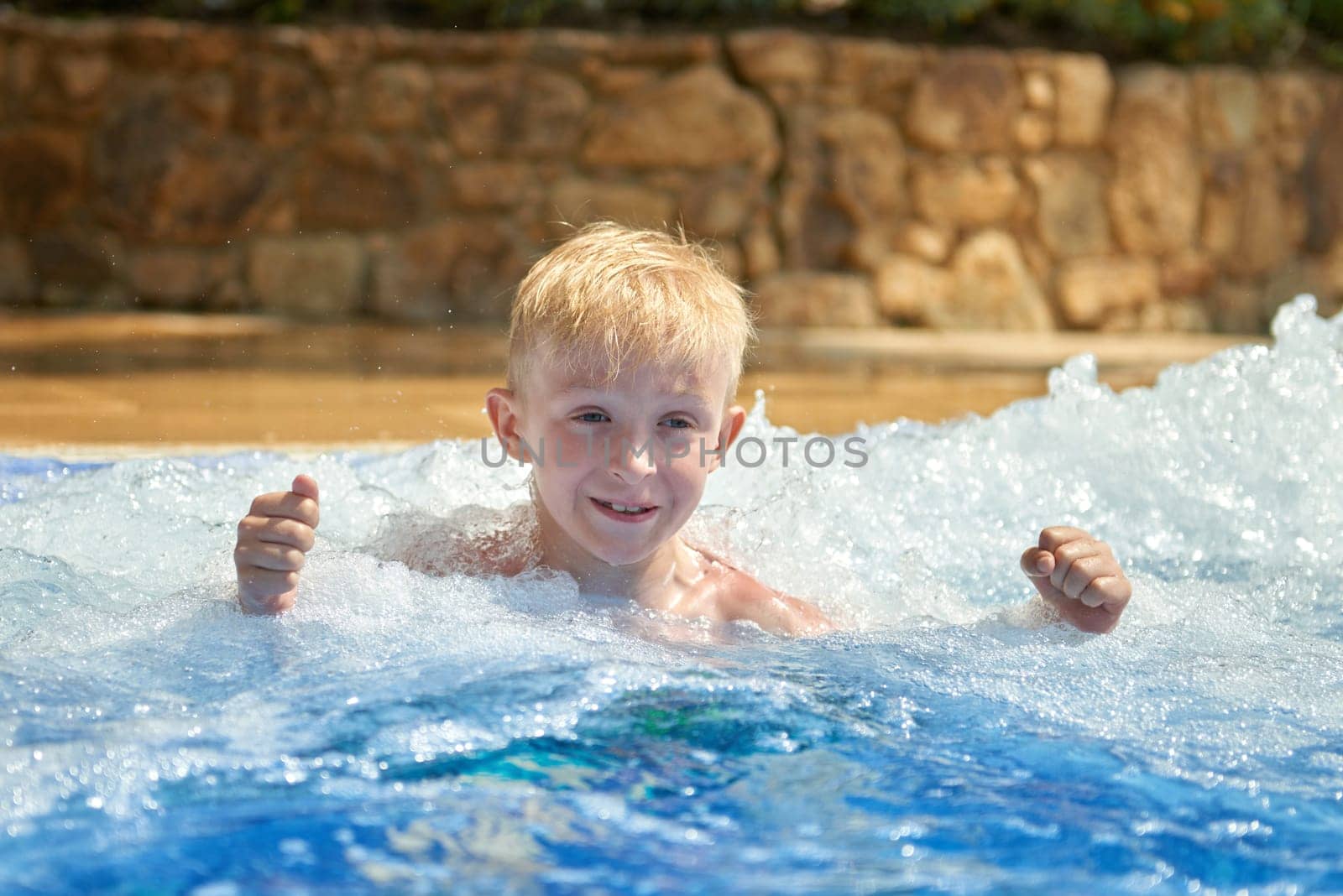 Young boy kid child eight years old splashing in swimming pool having fun leisure activity. Boy happy swimming in a pool. Activities on the pool, children swimming and playing in water, happiness and summertime.