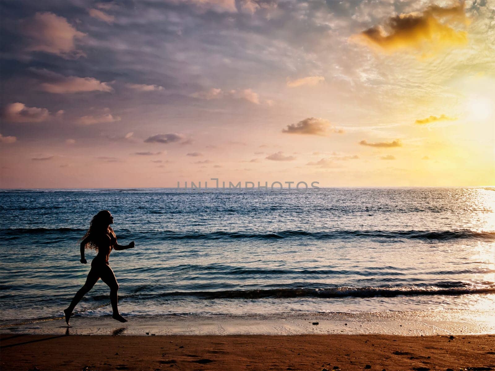 Beautiful athletic woman running along sea beach in the morning by dimol