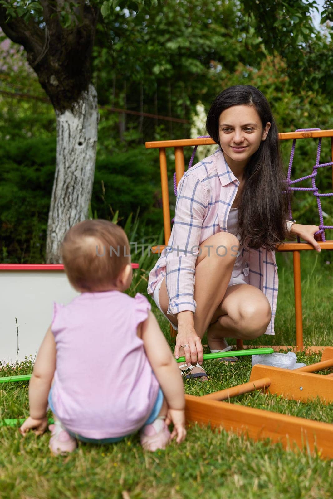 mother with little child girl daughter collects wooden home sports complex outdoor. assembly process