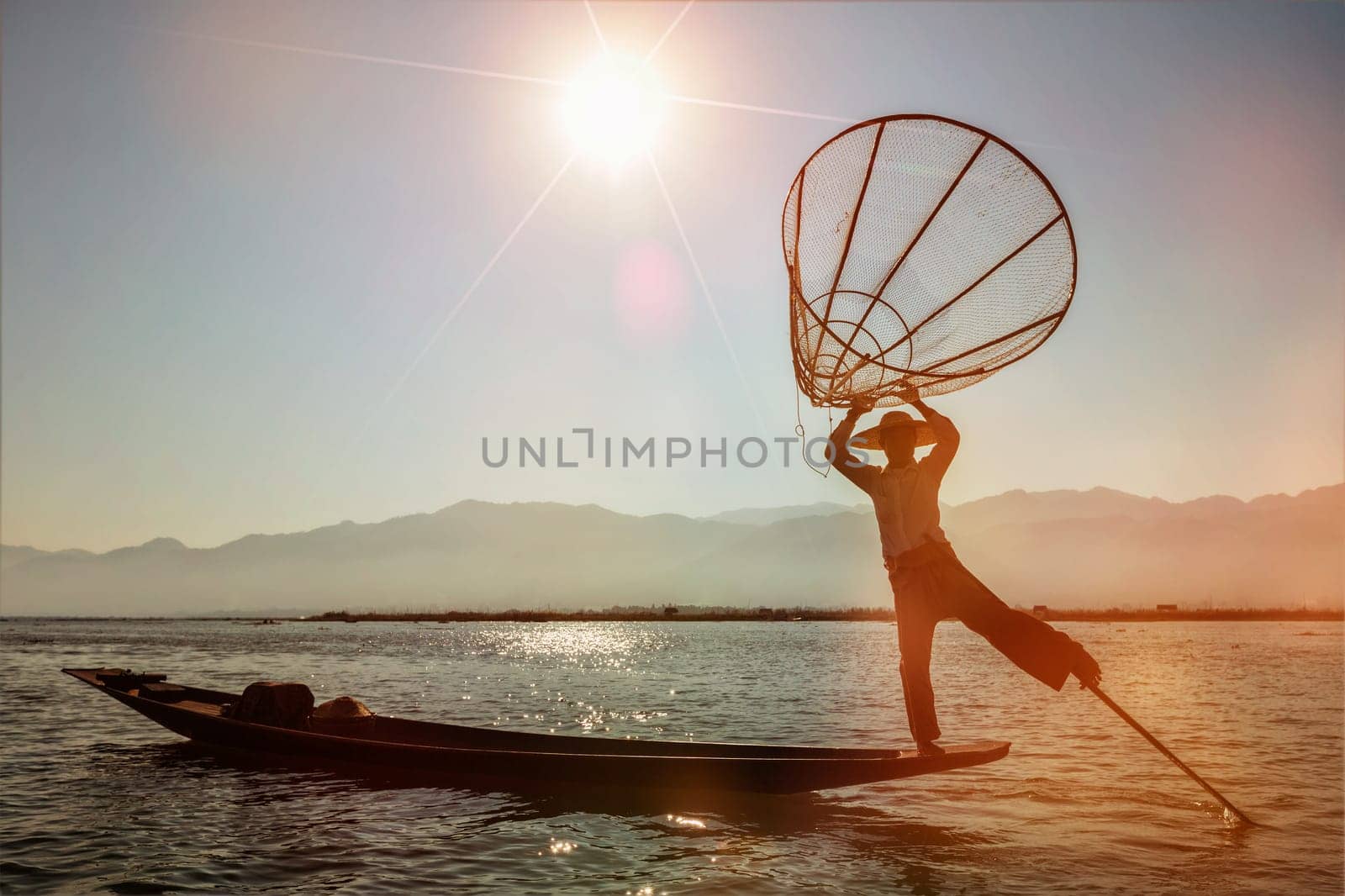 Myanmar travel attraction landmark - Traditional Burmese fisherman at Inle lake, Myanmar famous for their distinctive one legged rowing style on sunset. With light leak and lens flare