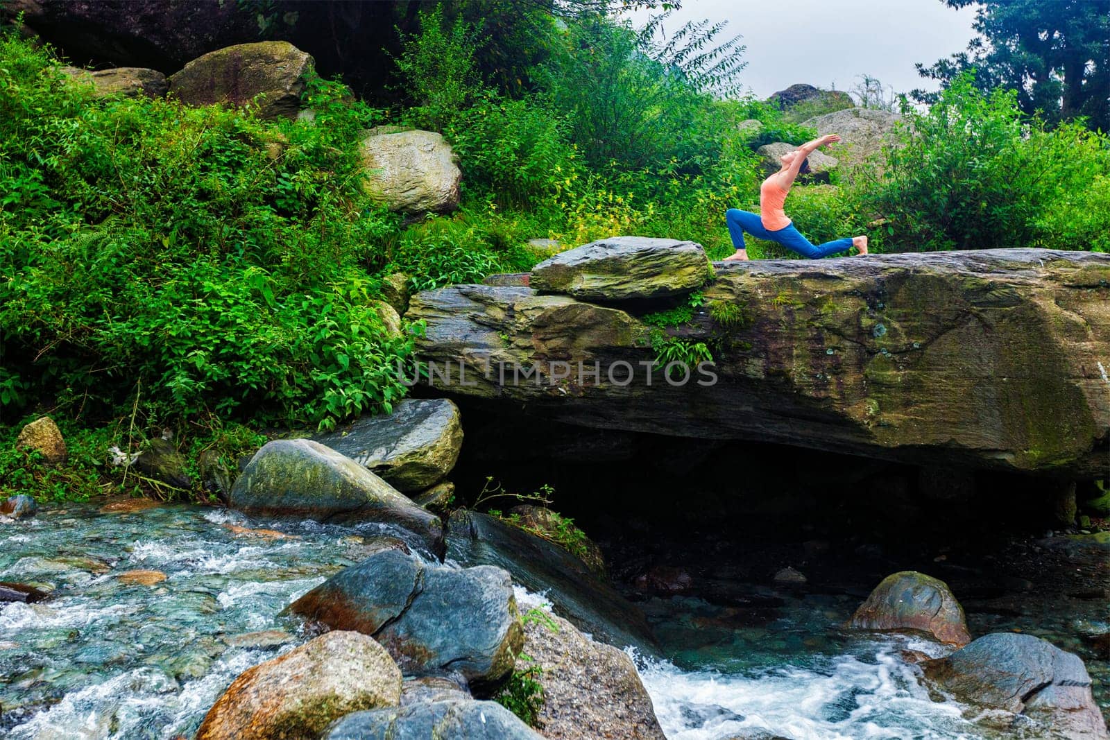 Sporty fit woman practices yoga Anjaneyasana in mountains by dimol