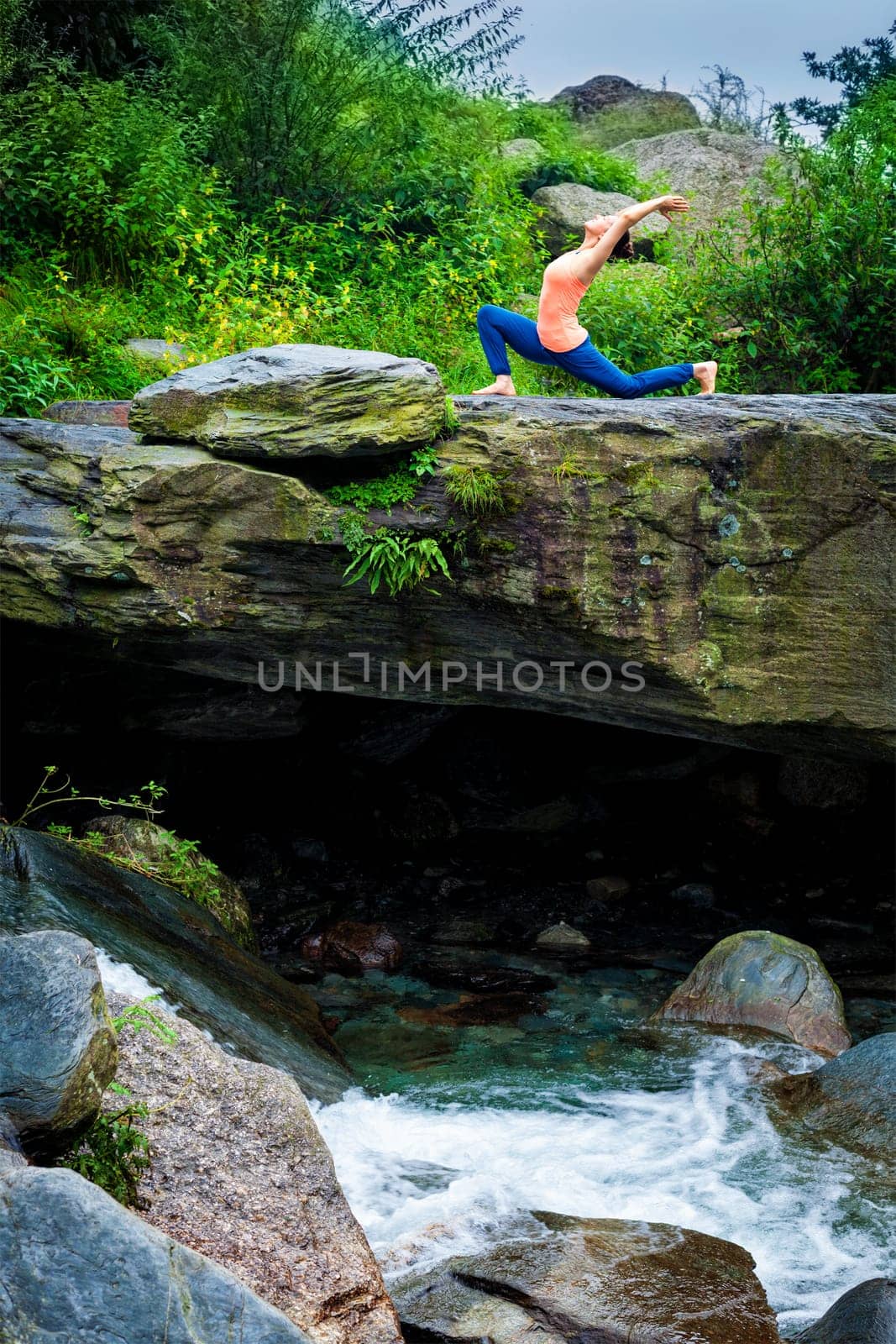 Yoga outdoors - sporty fit woman practices yoga Anjaneyasana - low crescent lunge pose outdoors in mountains