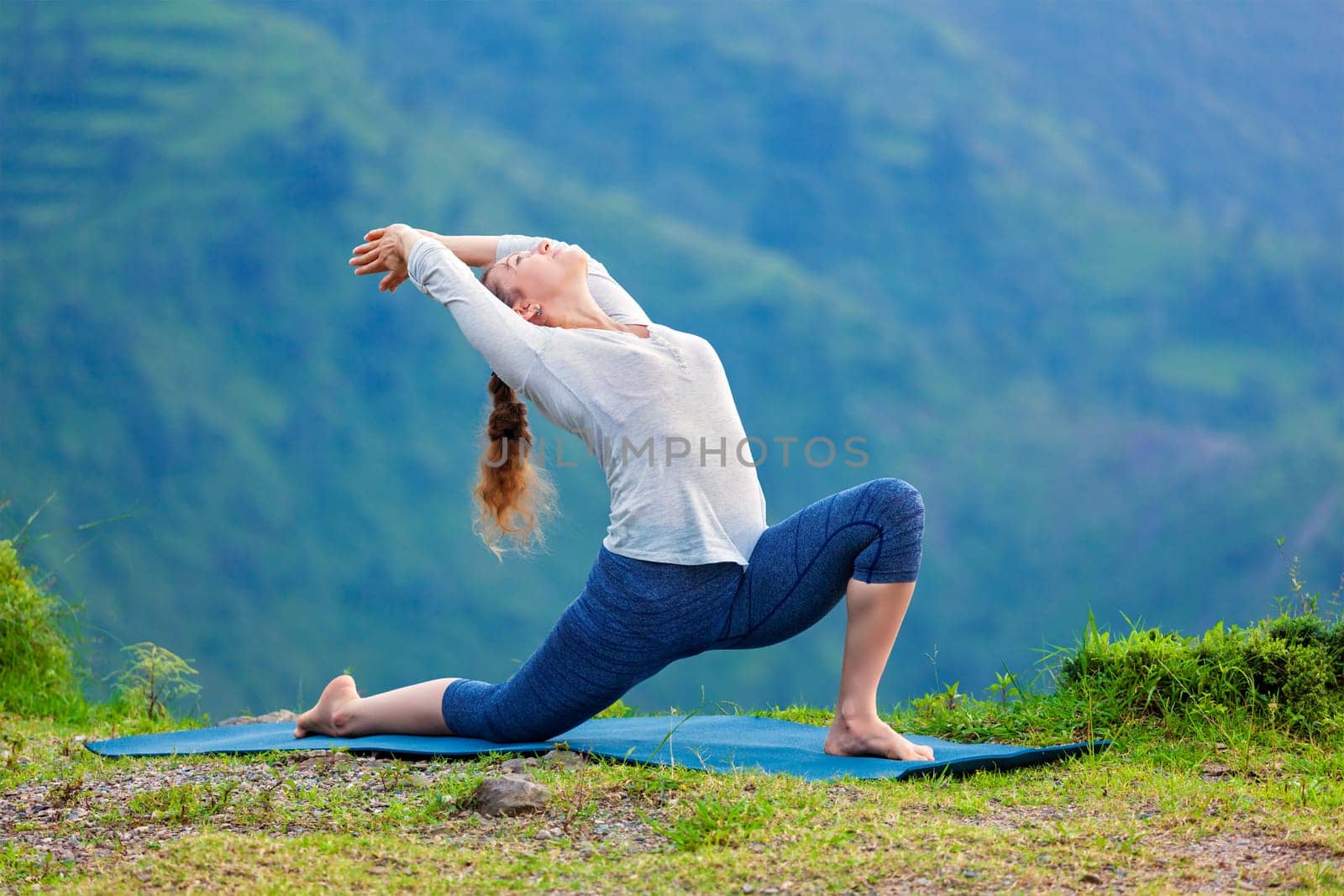 Sporty fit woman practices yoga asana Anjaneyasana in mountains by dimol