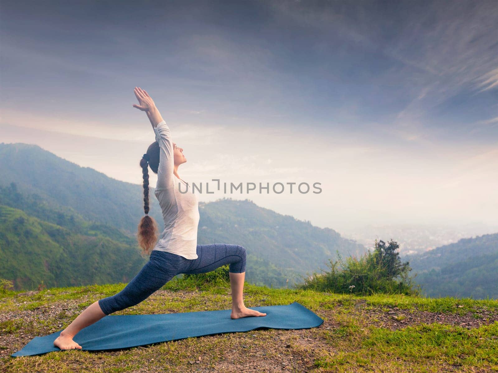 Yoga outdoors - sporty fit woman doing Ashtanga Vinyasa Yoga asana Virabhadrasana 1 Warrior pose posture in HImalayas mountains on sunset