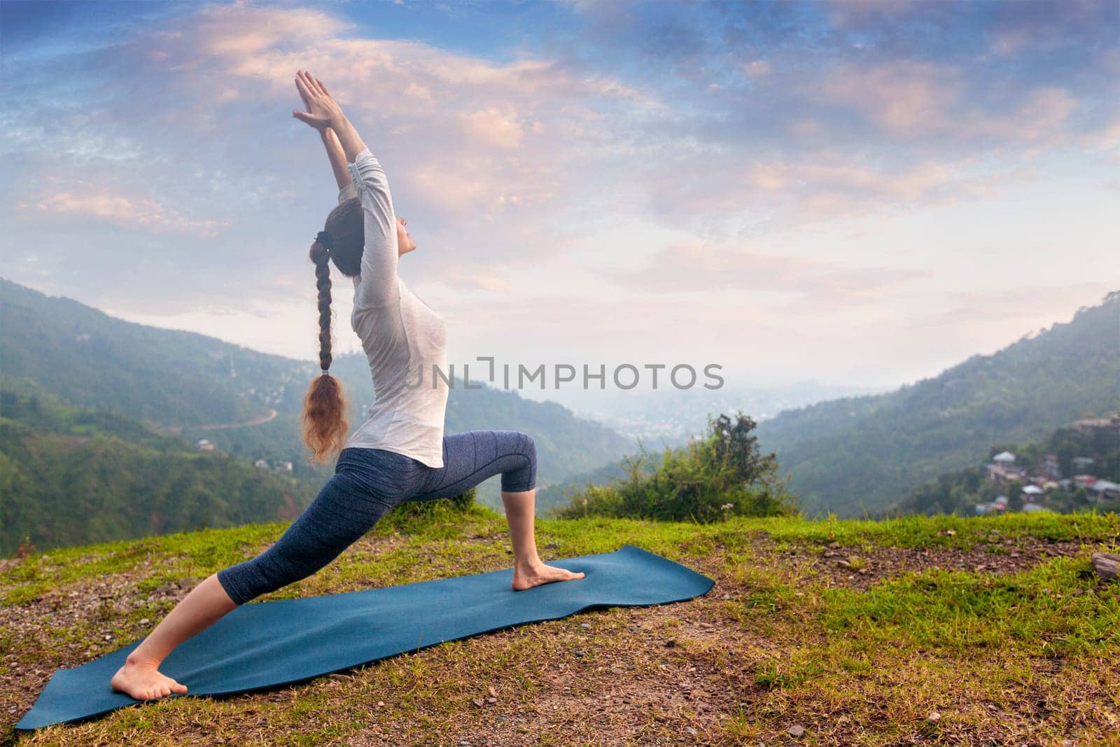 Yoga outdoors - sporty fit woman doing Ashtanga Vinyasa Yoga asana Virabhadrasana 1 Warrior pose posture in HImalayas mountains on sunset