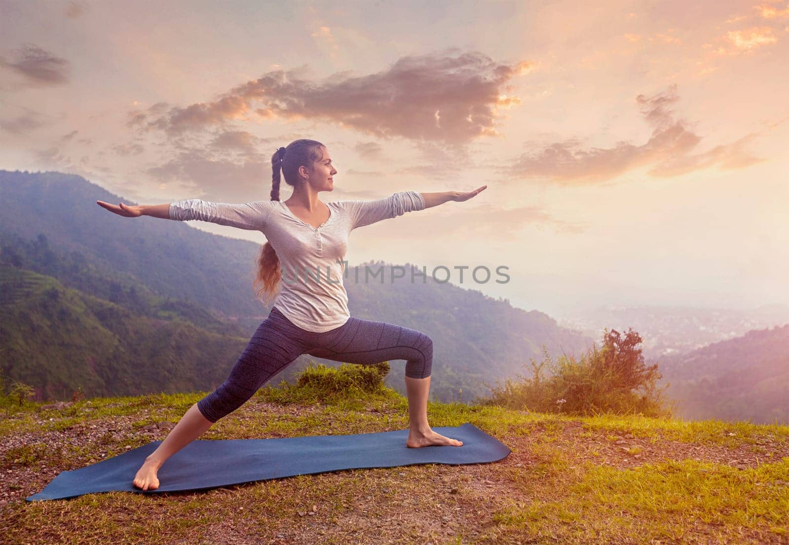 Yoga outdoors - sporty fit woman doing Ashtanga Vinyasa Yoga asana Virabhadrasana 2 Warrior pose posture in mountains