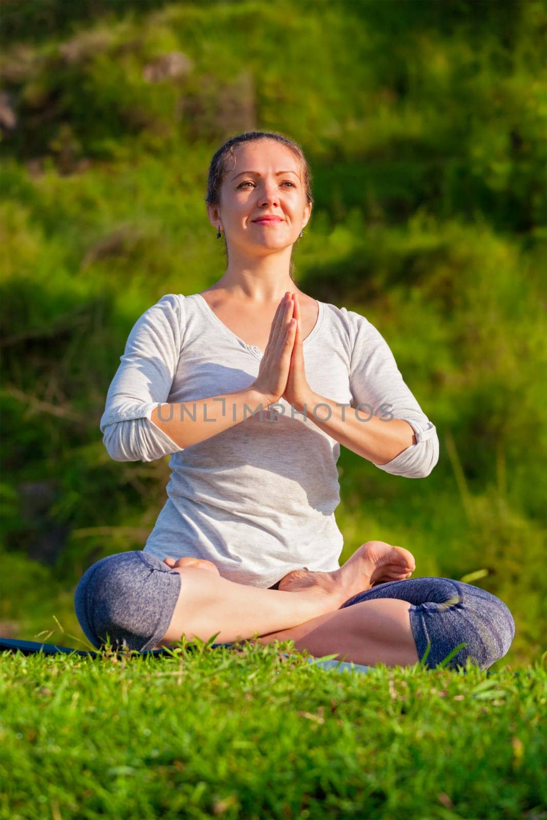 Young sporty fit woman doing yoga Lotus pose oudoors by dimol