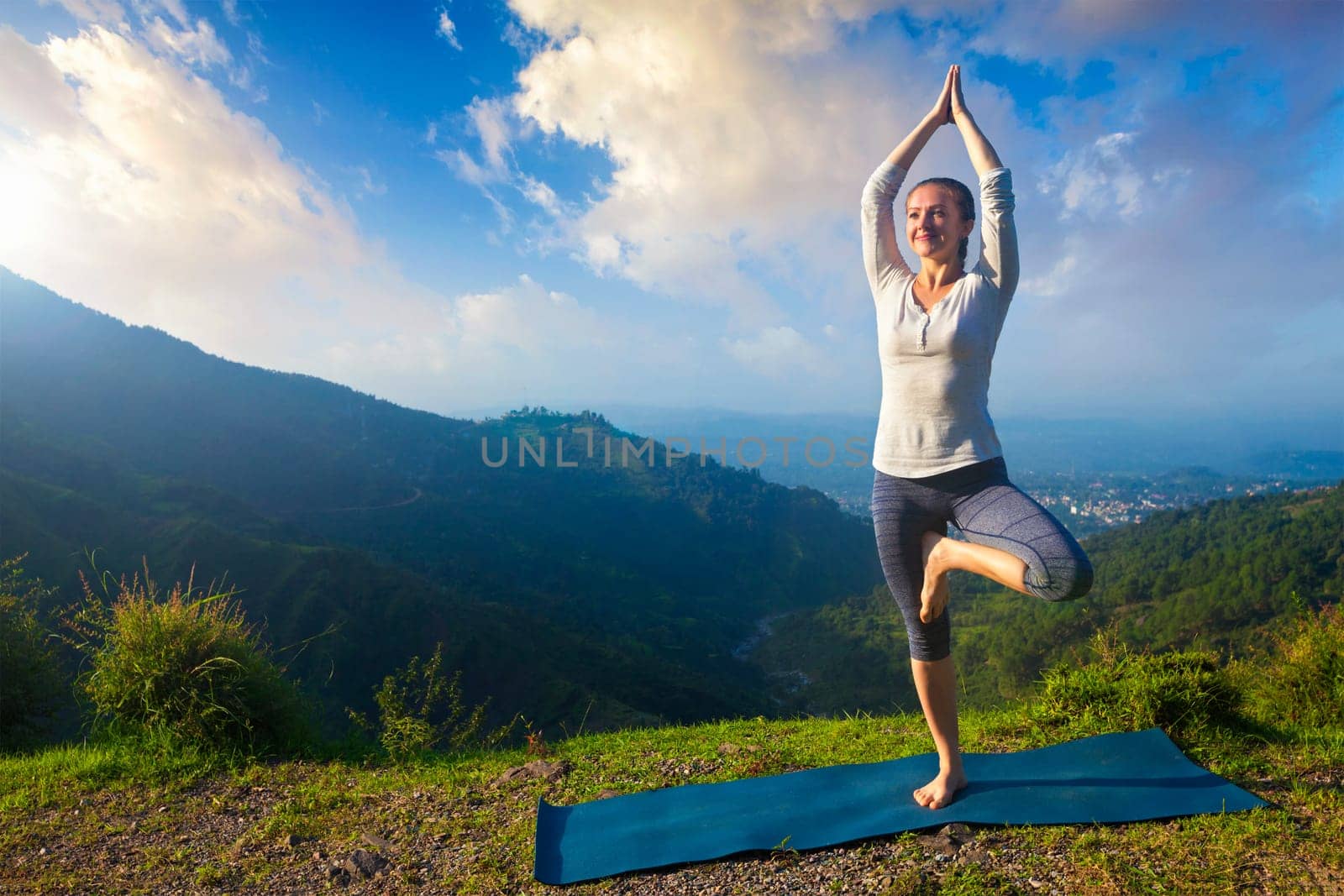 Woman in yoga asana Vrikshasana tree pose in mountains outdoors by dimol