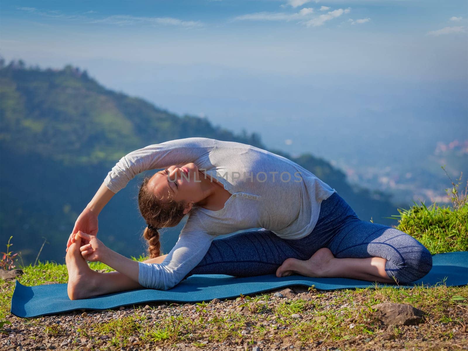 Yoga outdoors - young sporty fit woman doing Hatha Yoga asana parivrtta janu sirsasana - Revolved Head-to-Knee Pose - in mountains in the morning