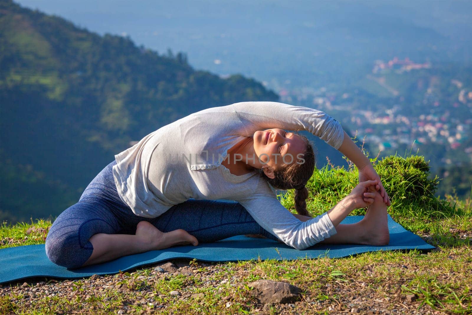 Yoga outdoors - young sporty fit woman doing Hatha Yoga asana parivrtta janu sirsasana - Revolved Head-to-Knee Pose - in mountains in the morning