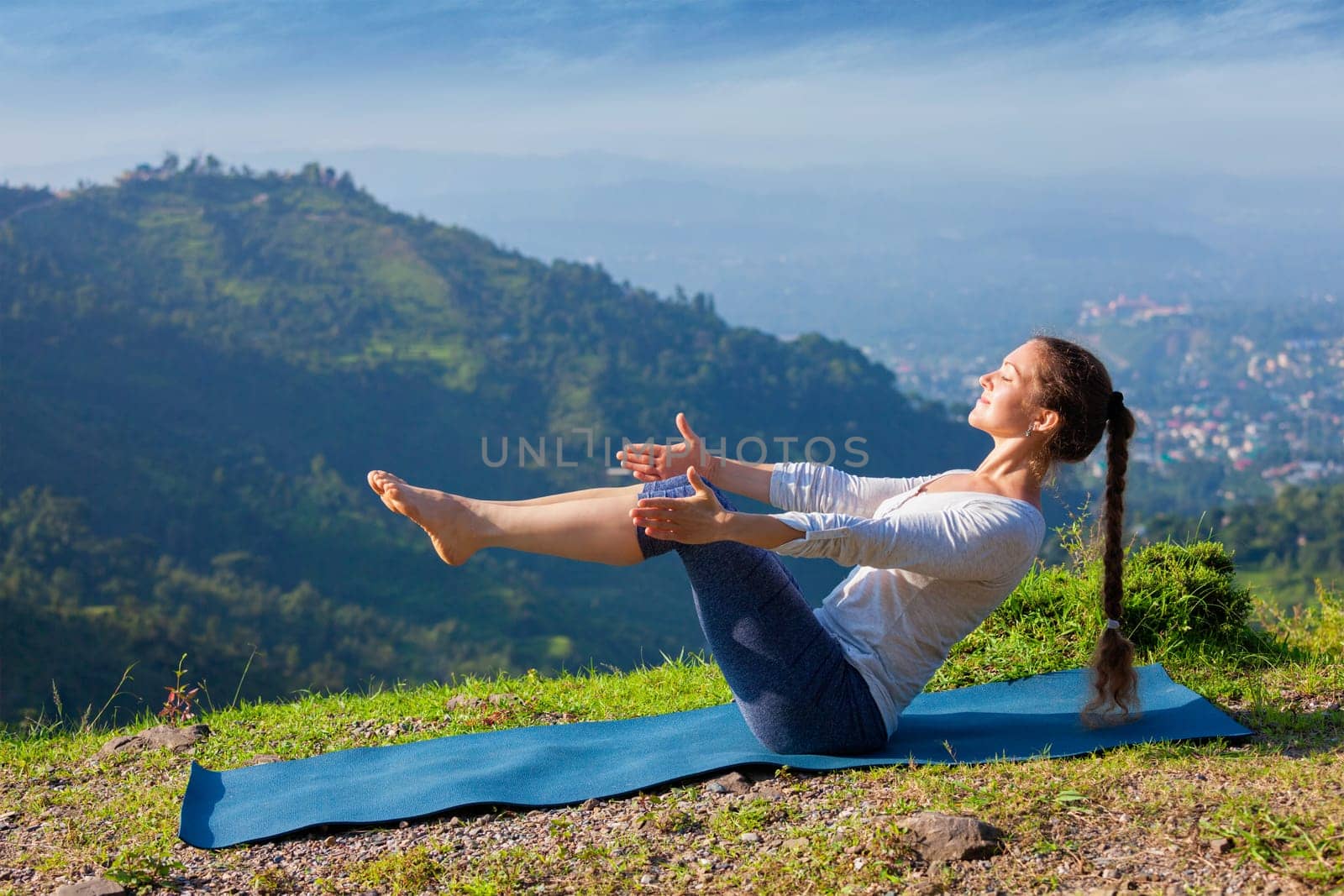 Yoga outdoors - young sporty fit woman doing Ashtanga Vinyasa Yoga asana Navasana - boat pose easy beginner variation - in Himalayas mountains in the morning Himachal Pradesh, India