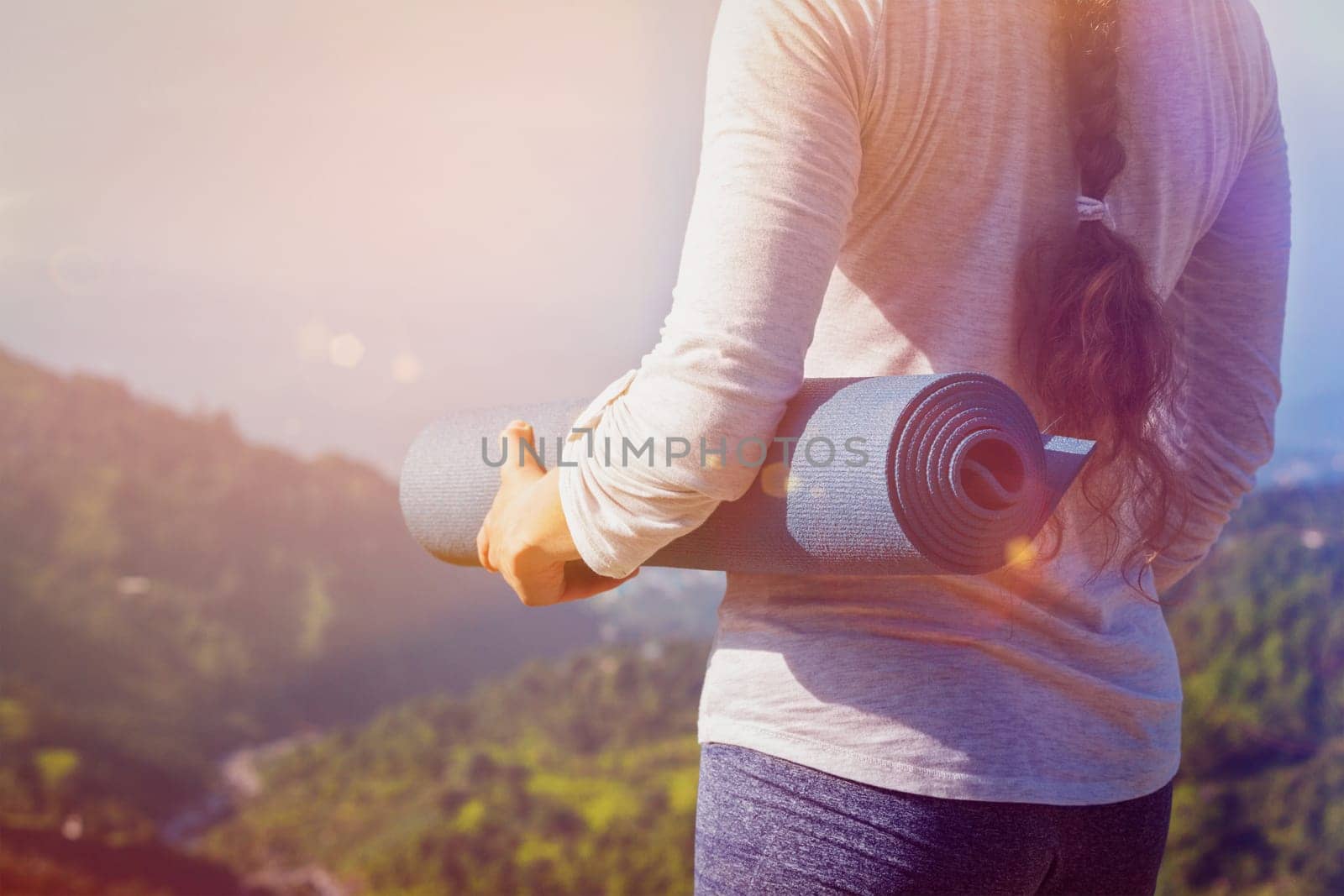Woman standing with yoga mat outdoors in mountains close up with copyspace. With light leak and lens flare