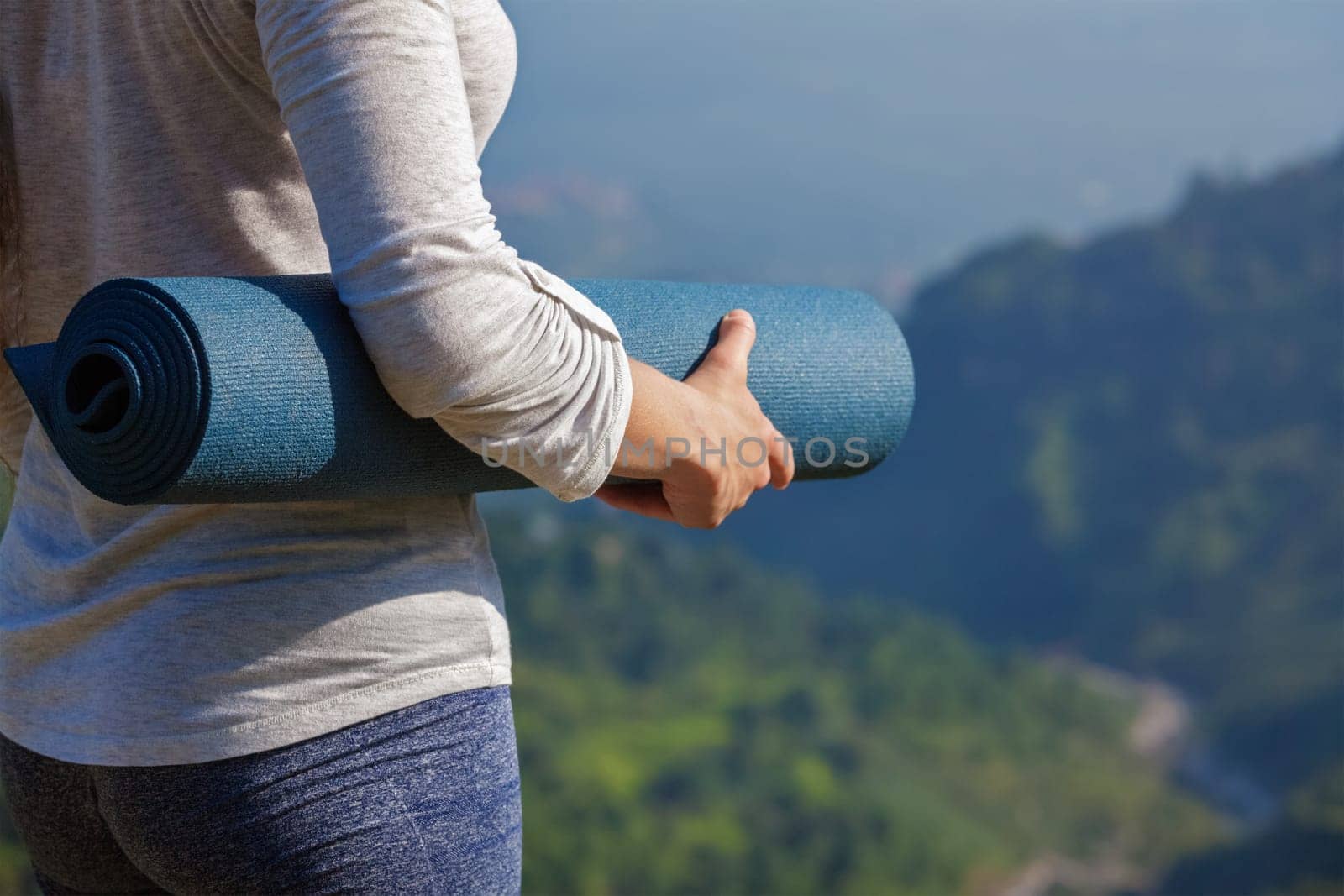 Woman standing with yoga mat outdoors in mountains close up with copyspace getting ready for yoga exercise
