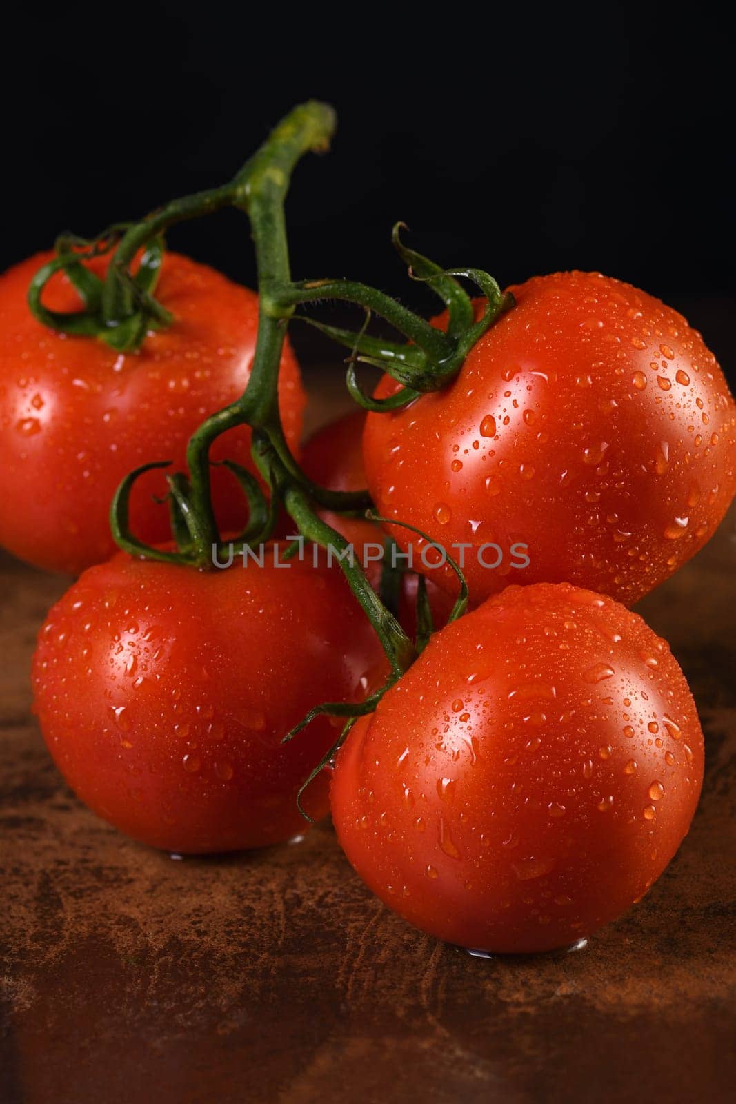 Fresh ripe red tomato branch on a rusty, redhead table with water drops. Dark background. Close-up. Vertical photo. Poster for vegetable market or shop.