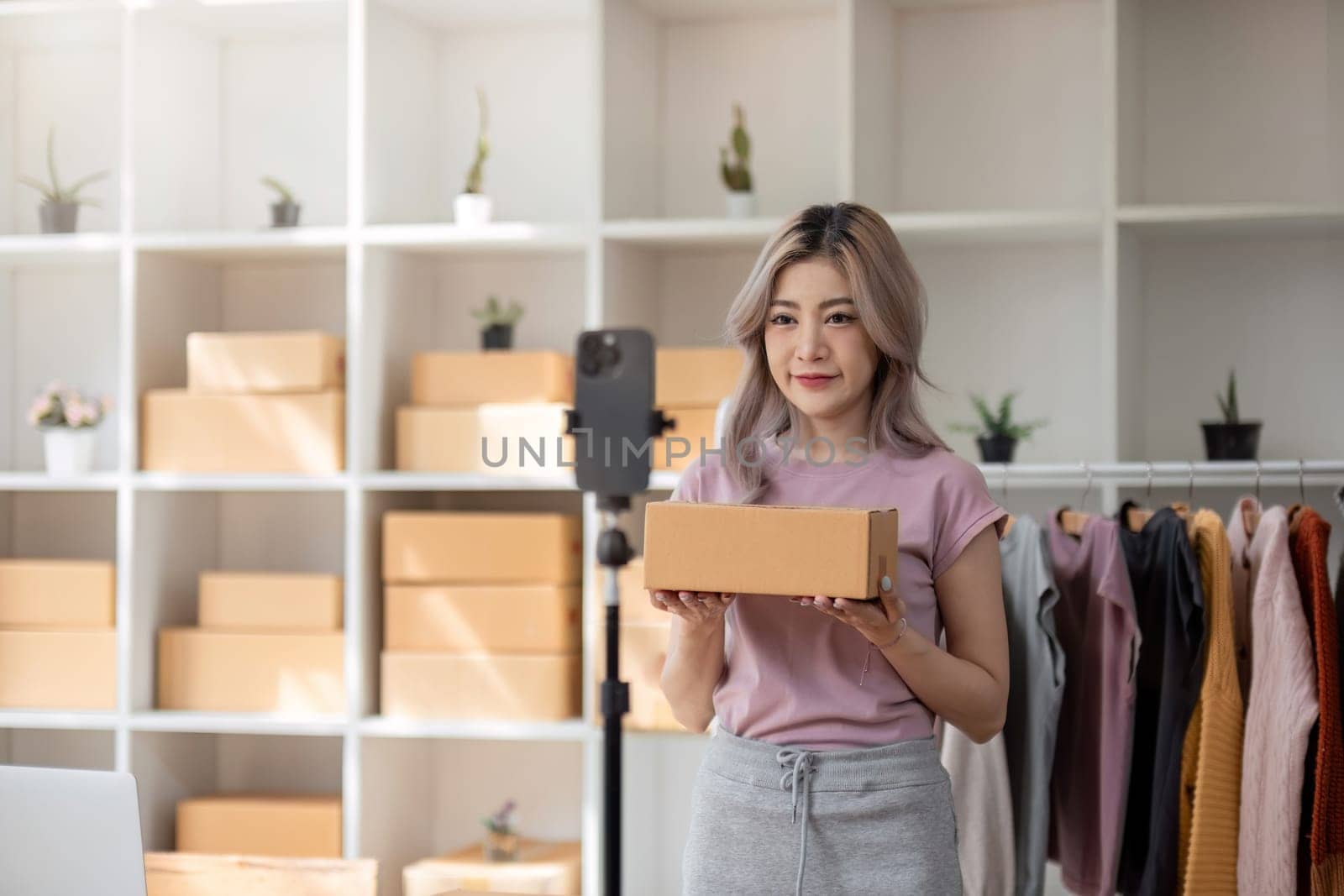 Blogger small SME business woman using mobile phone video call for sell clothes live stream selling online, show product present detail at home office, entrepreneur ecommerce.