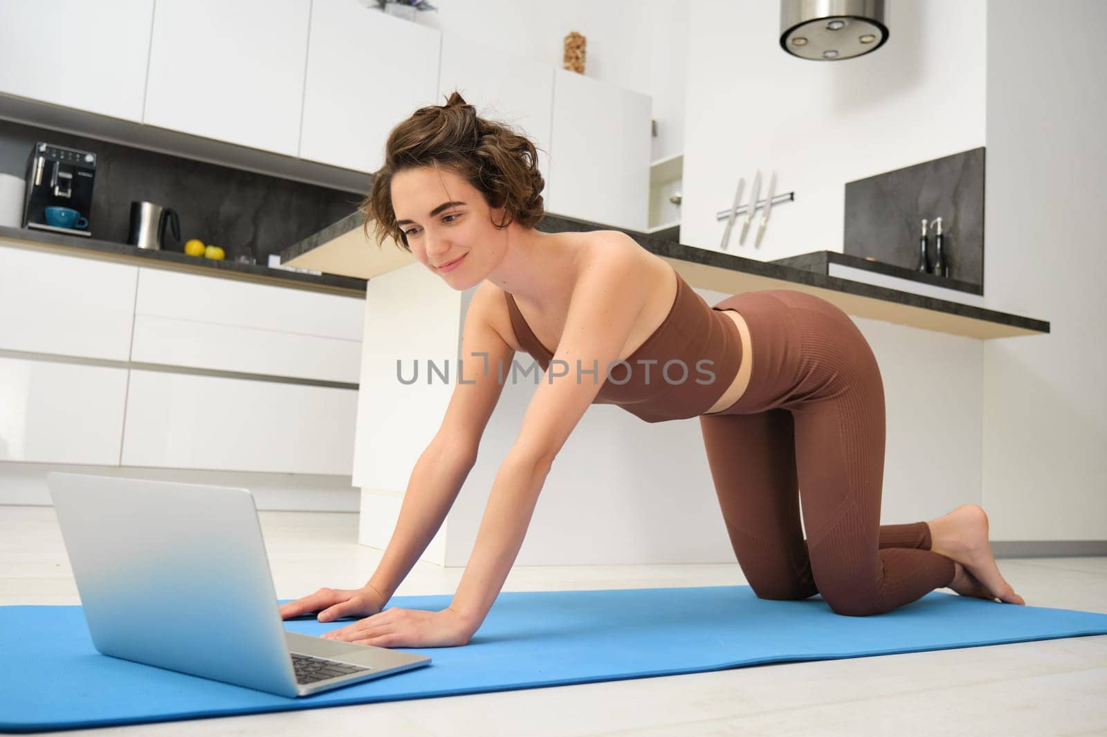 Sportswoman standing on rubber mat and watching online workout videos on laptop, workout from home with yoga computer application.