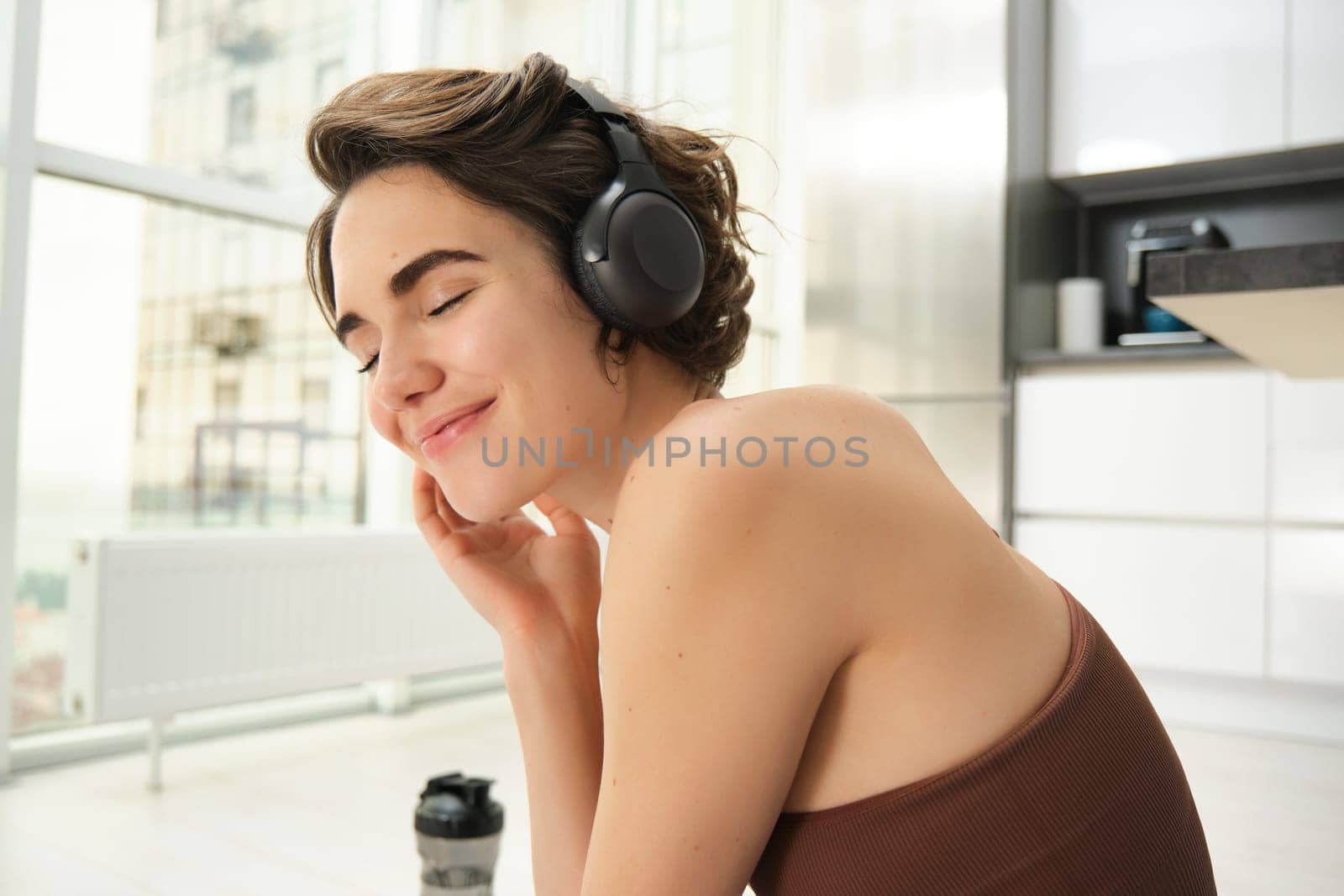 Close up portrait of young smiling woman, fitness girl in headphones, listens music and does workout training at home, exercise indoors, practice yoga and pilates.