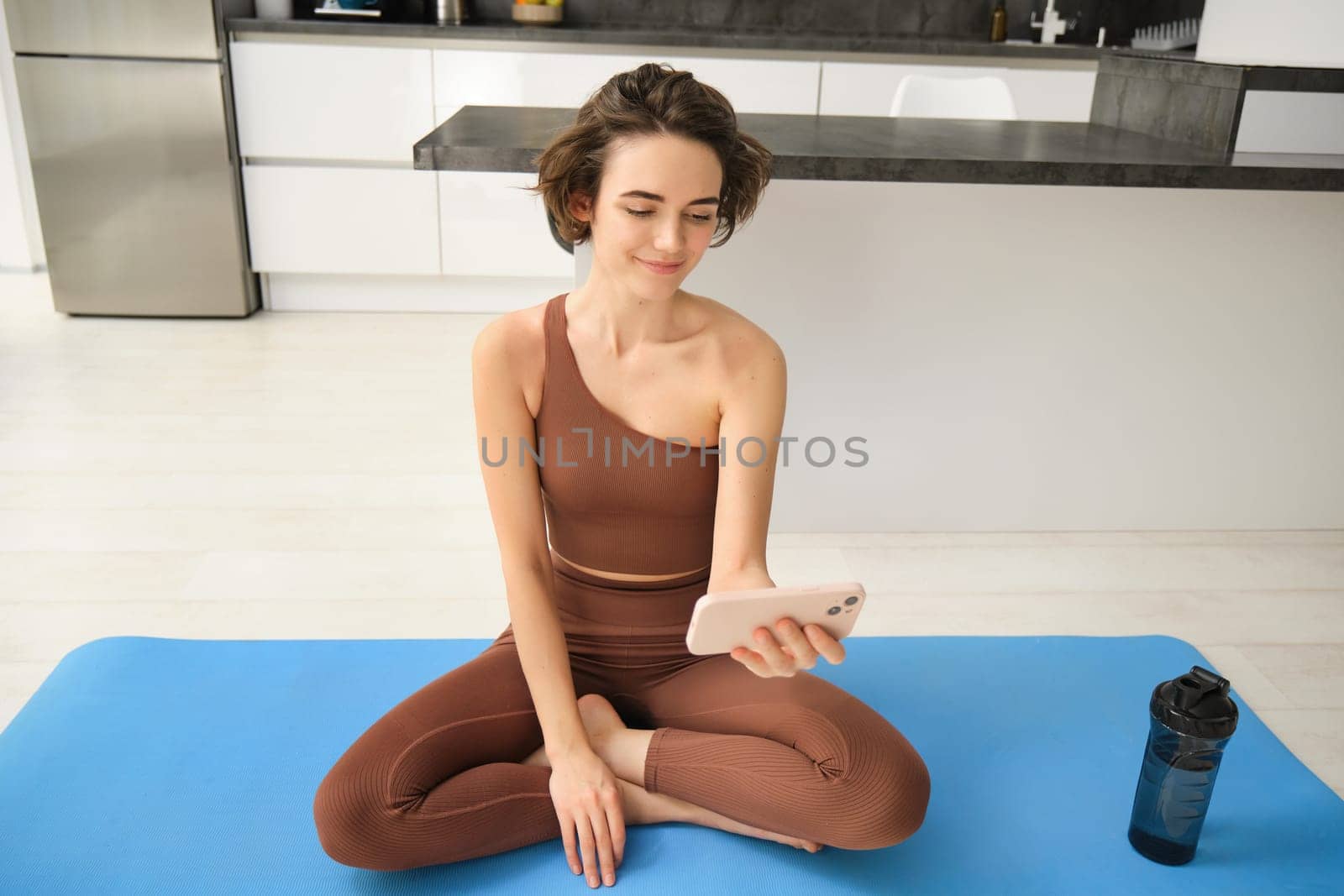 Portrait of young girl athelte, sportswoman sits at home, watching yoga, fitness video tutorials, workout alone indoors on rubber mat. Sport and lifestyle concept