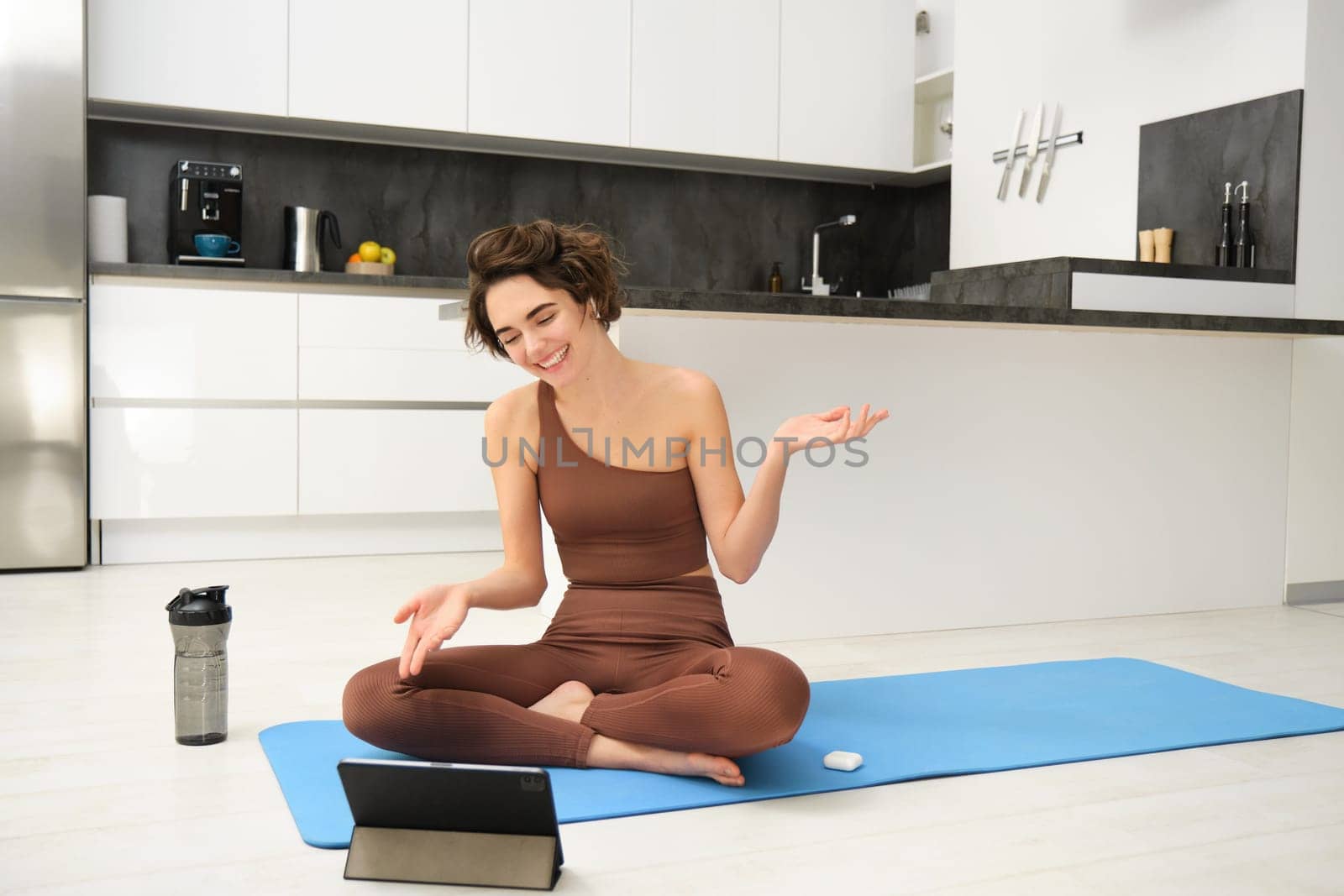 Woman, fitness instructor sitting on rubber mat, yoga couch talking to online group, recording class on tablet, remote training outside of gym, workout from home by Benzoix