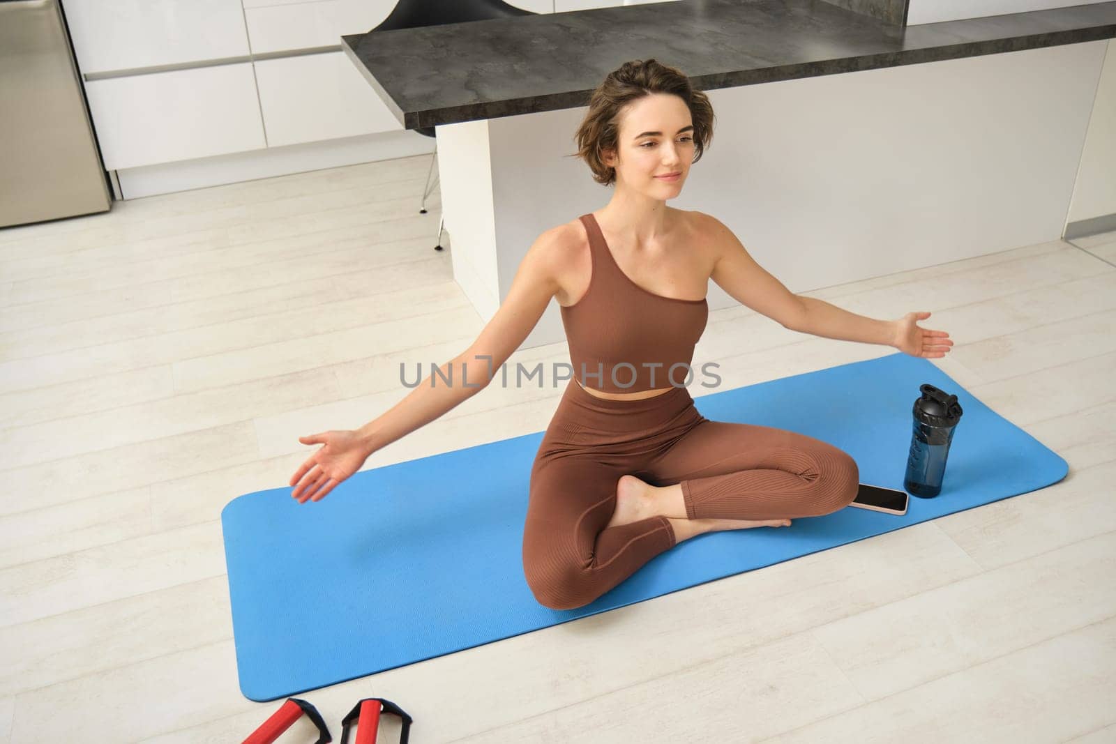 Young calm fit healthy woman wearing sportswear sitting at home in living room doing yoga exercise, meditating and breathing in the morning. Mental health and zen meditation concept.