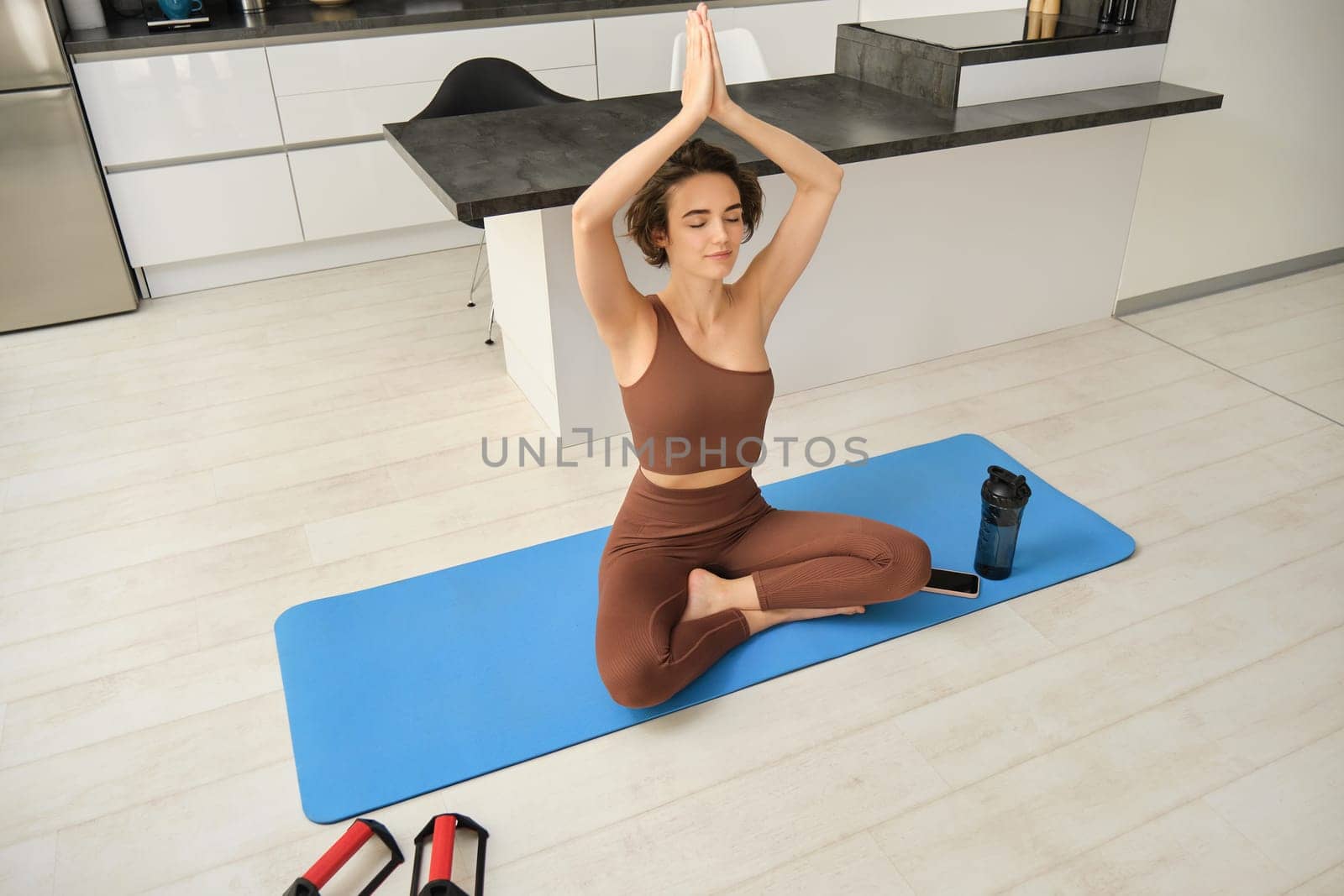 Portrait of fit and healthy woman in sportswear, doing yoga at home on fitness mat, making asana, relaxing and meditating indoors.