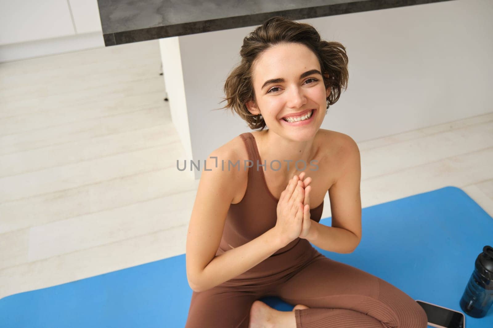 Peace, mindfulness and meditation. Young smiling sportswoman, fitness girl sits at home on floor and meditating, doing yoga, relaxing in lotus pose.