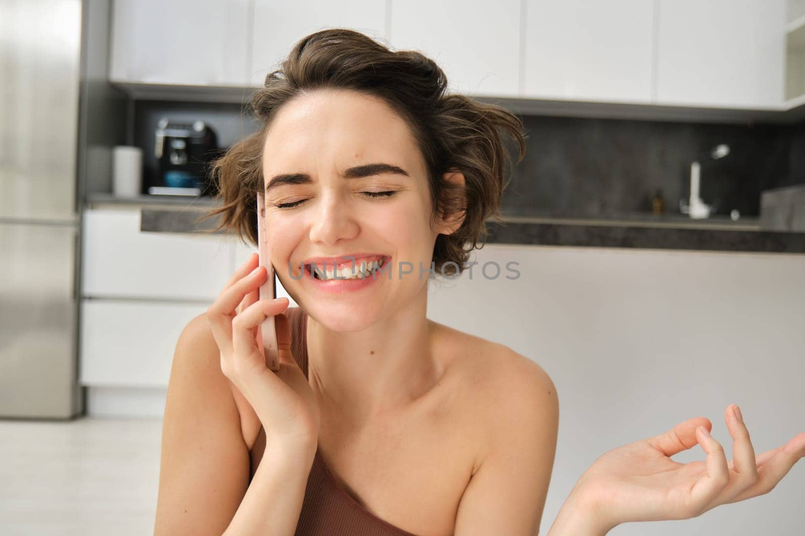 Close up portrait of happy smiling woman talking on mobile phone from her kitchen. Chatty girl with smartphone, laughing, calling someone. Lifestyle and women concept