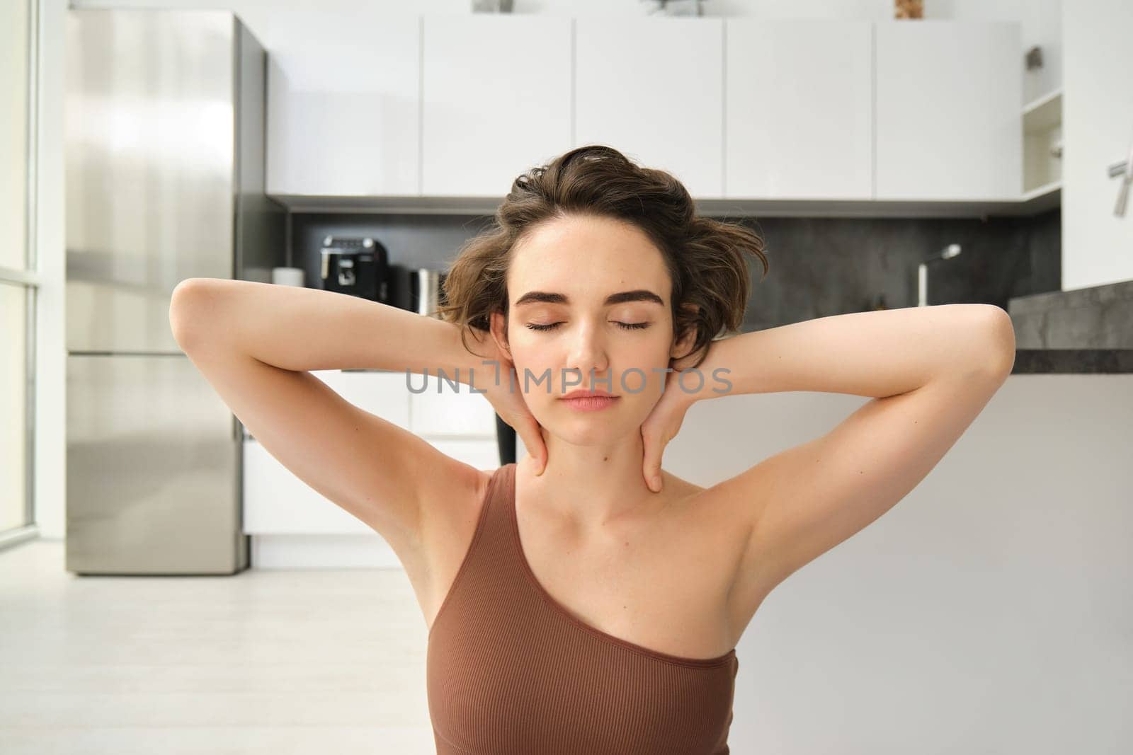 Home sports and wellbeing. Young brunette woman in sportswear, staying at home and doing yoga, mindful exercises, sitting in yoga pose with eyes closed and relaxed face. Copy space