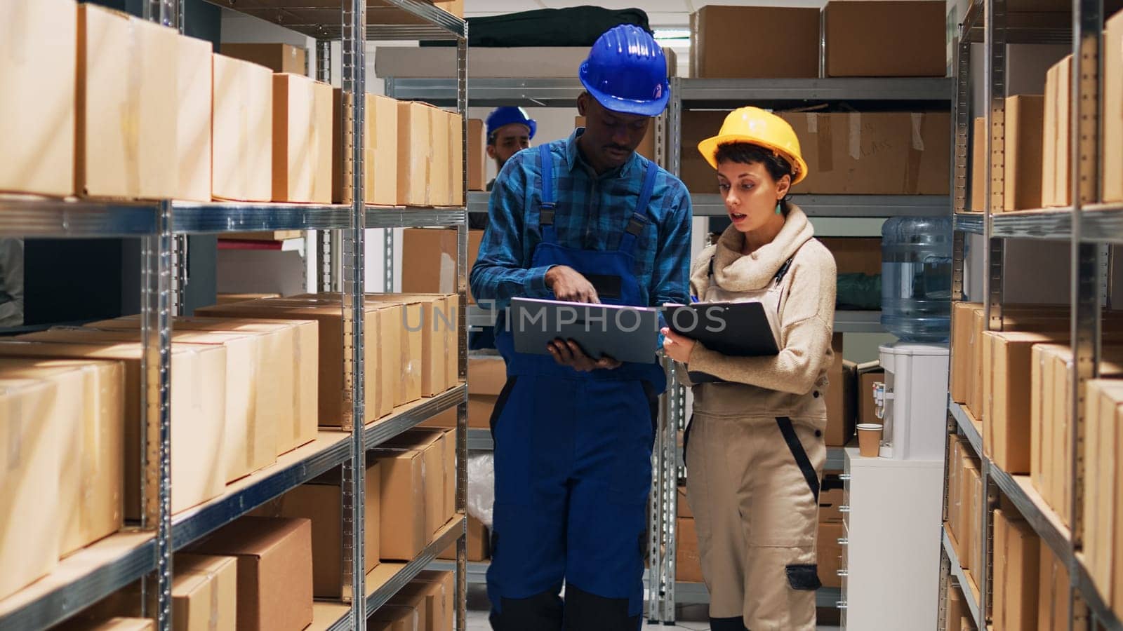 Multiethnic team of employees working with goods and checking stock inventory on laptop, cargo in storage room. Depot workers analyzing industrial goods to plan distribution and shipment.