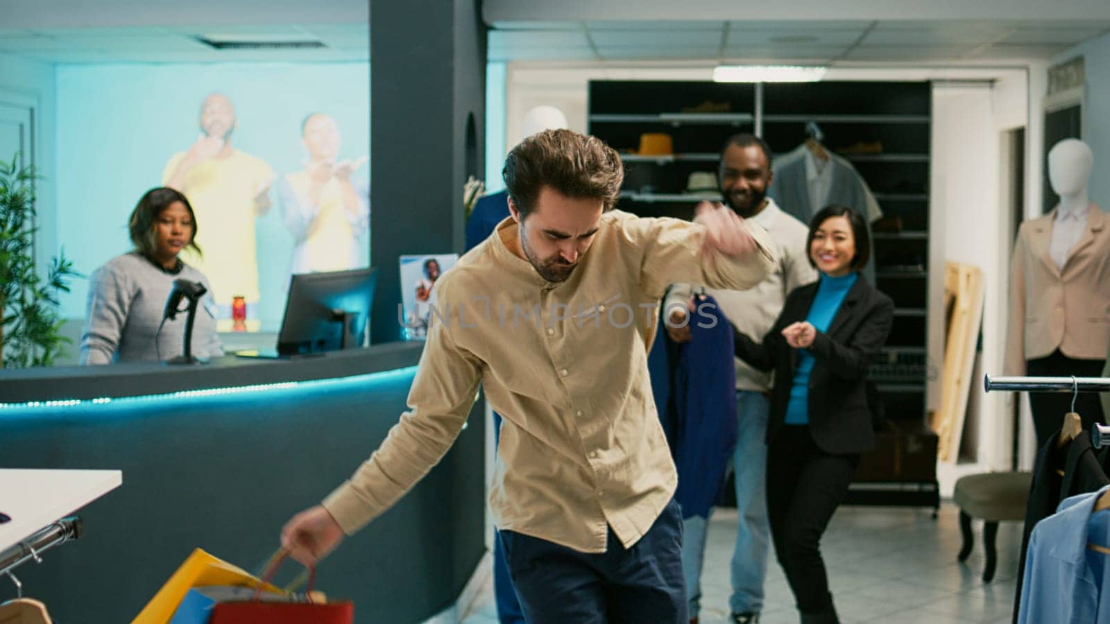 Happy man dancing in clothing store with shopping bags, enjoying fashion boutique merchandise at mall. Young client being silly with dance moves, feeling cheerful at cash register.