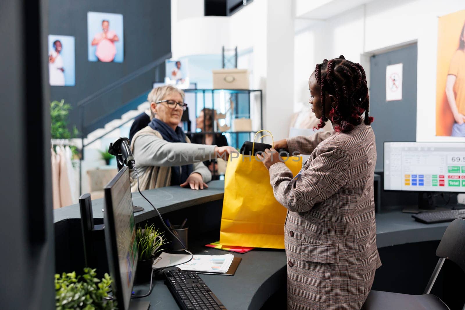 African american showroom worker preparing purchase for elderly client in clothing store. Shopaholic woman buying fashionable casual wear, making electronic payment at pos terminal.