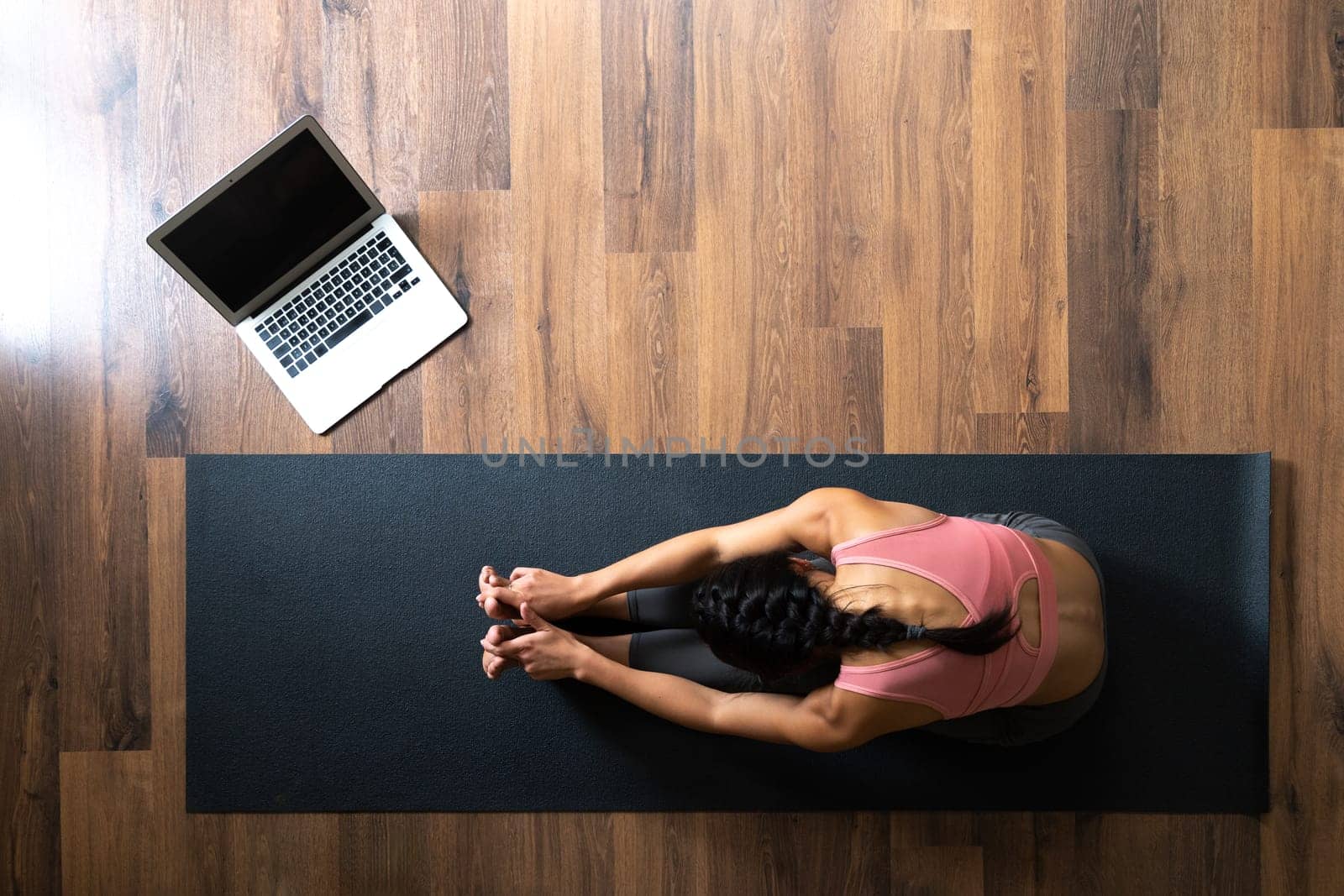Top view of female doing yoga stretching exercise following online classes at home. Copy space. by Hoverstock