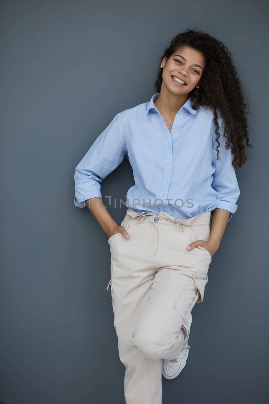 Smiling attractive young business woman in blue shirt posing on gray background by Prosto