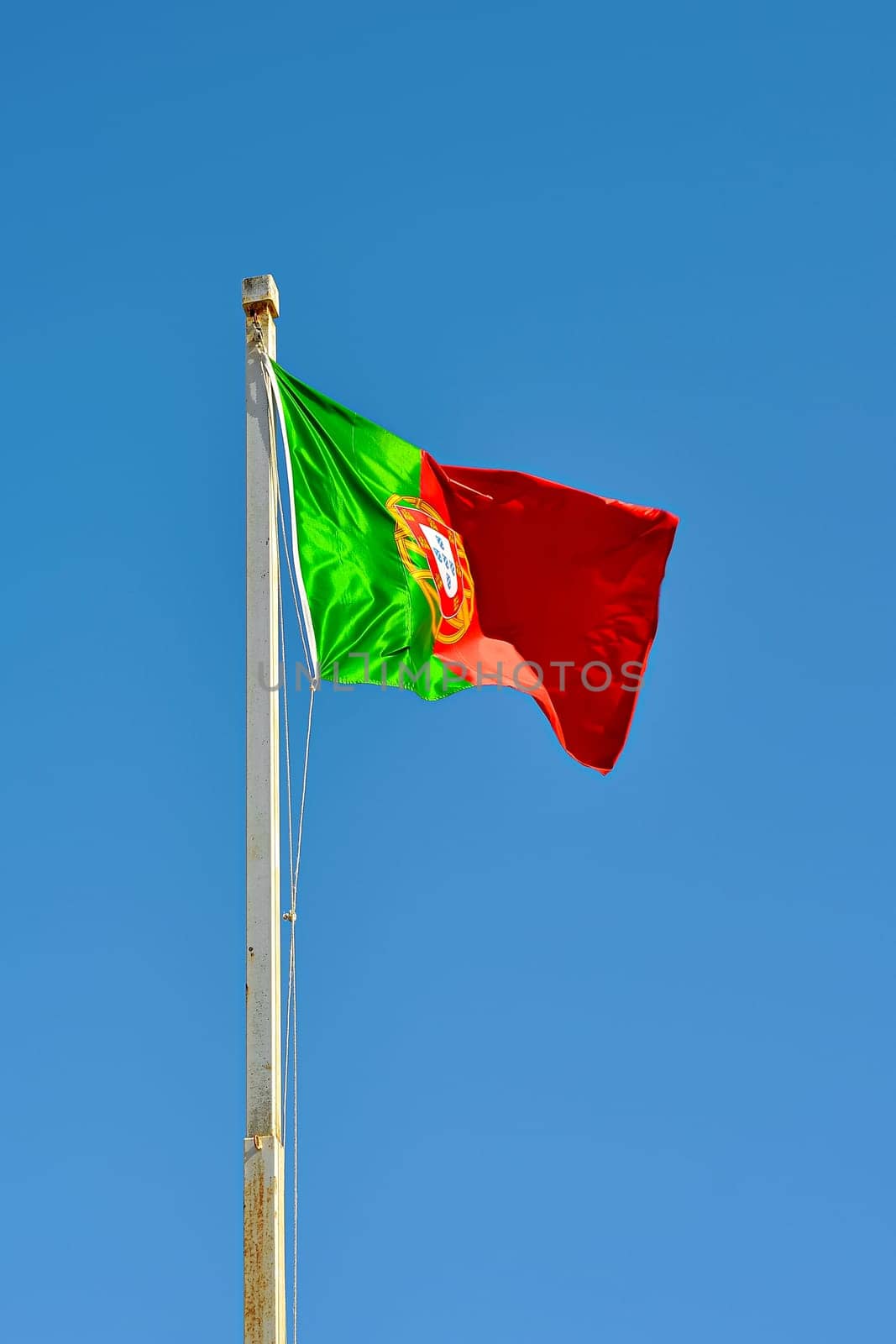 Portuguese flag waving in the wind against blue sky. Portuguese Flag Waving Against Blue Sky. Flag of Portugal waving, against blue sky vertical banner.