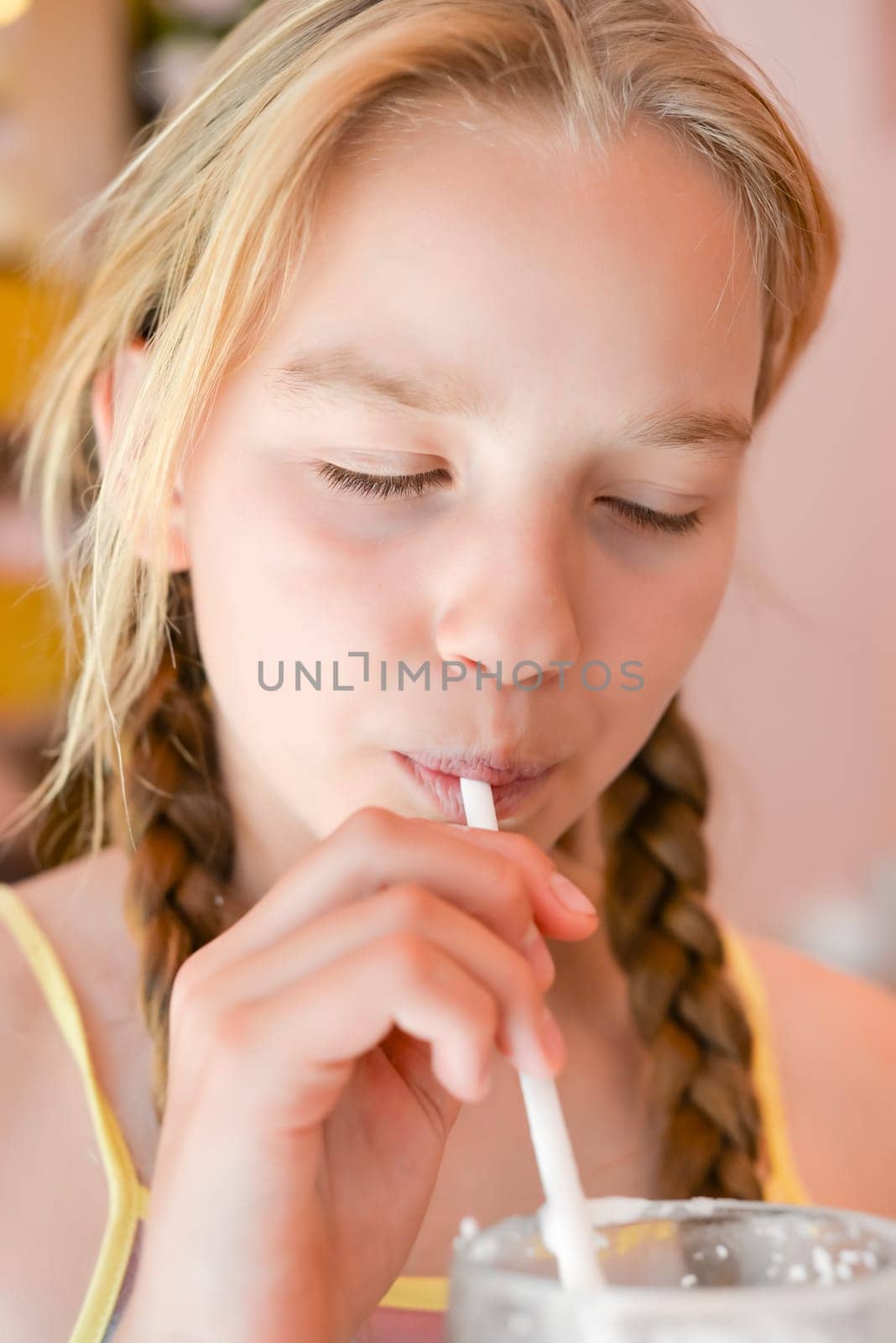 Teen pretty girl eleven years old drinking strawberry milkshake through a straw in a coffee shop. Portrait of The happy girl drinking a cocktail through a straw.