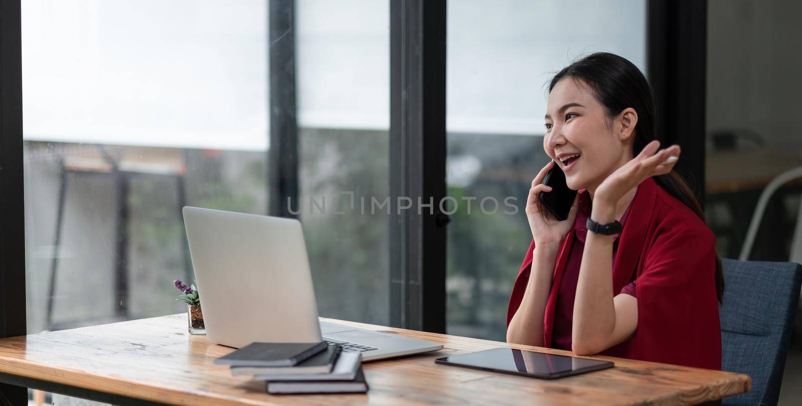 Portrait young asian businesswoman beautiful charming smiling and talking on the mobile phone in the office. female working with laptop computer by nateemee