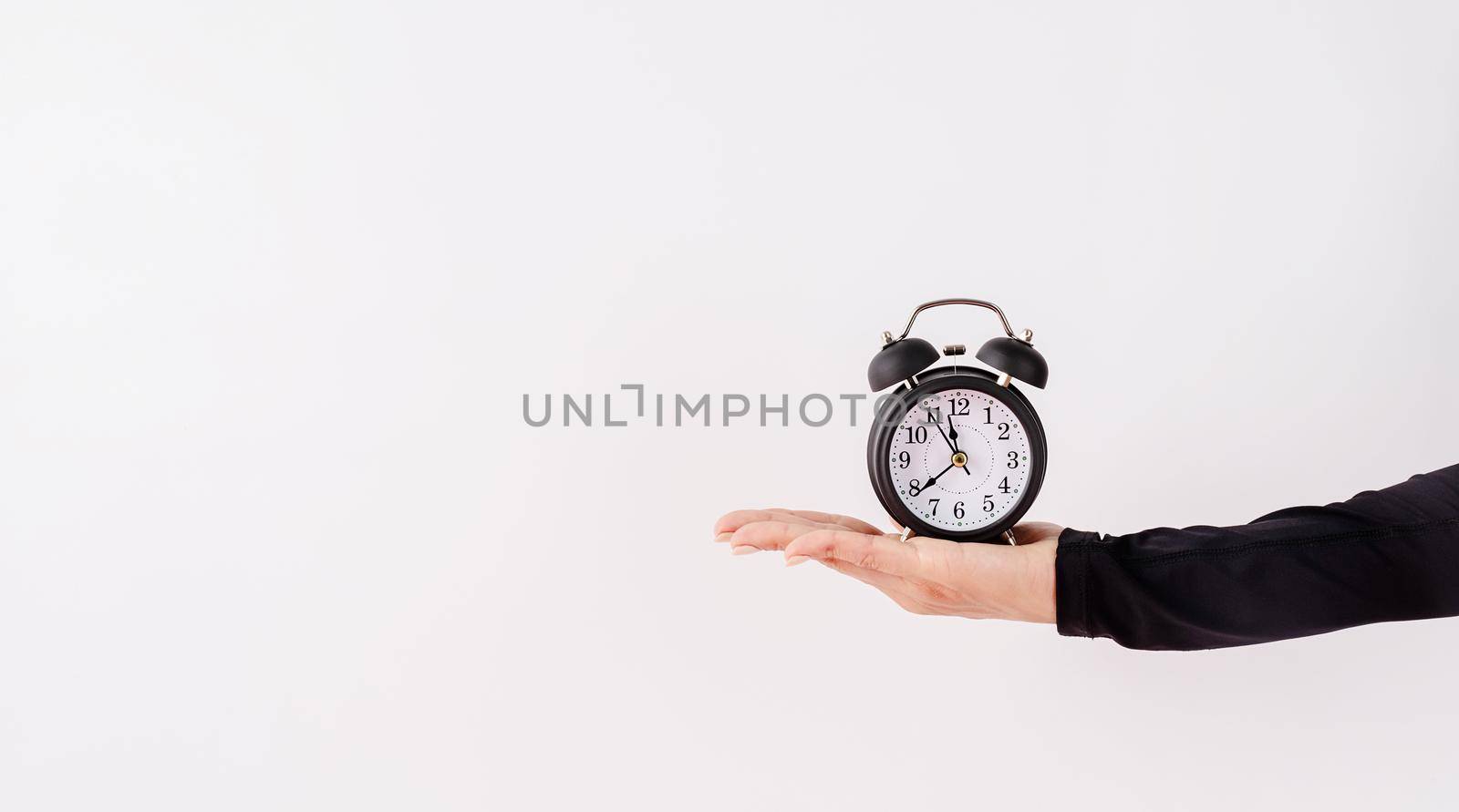 Time management, punctuality, business metaphors. Female hand holding white alarm clock on white background with copy space