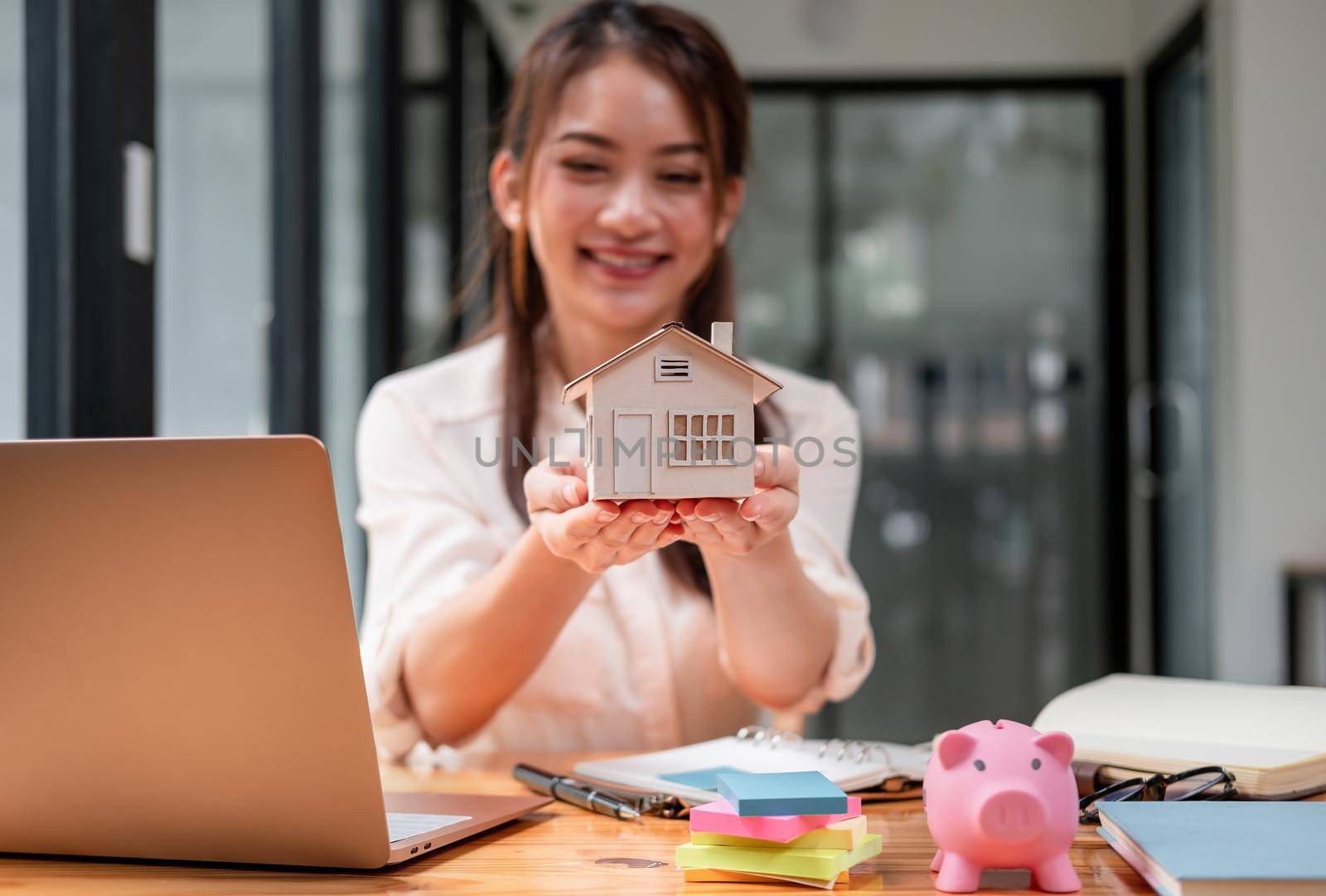 Real estate woman hands holding house model presenting to client with piggy bank on desk. money saving sell or buy house concept.