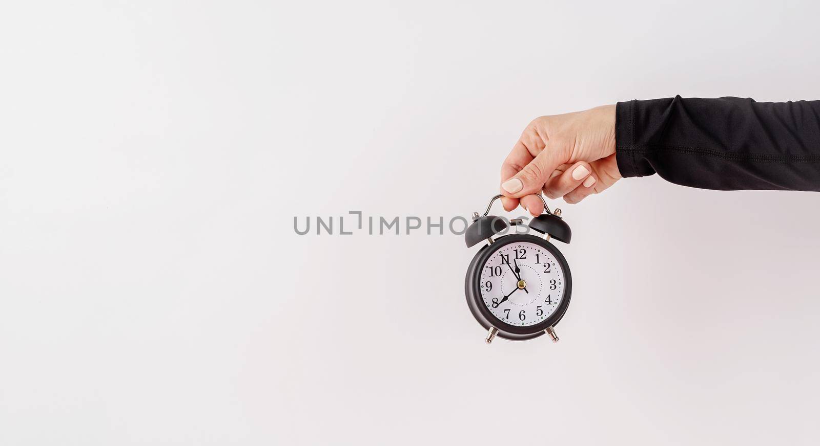 Time management, punctuality, business metaphors. Female hand holding white alarm clock on white background with copy space