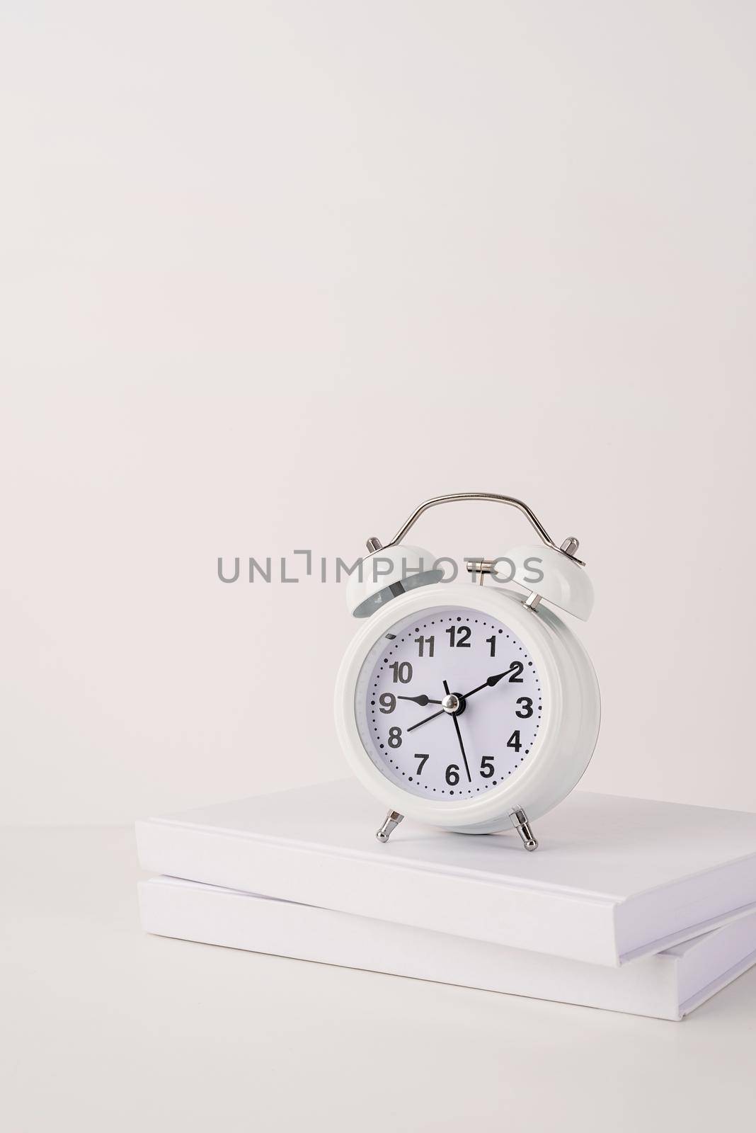 Time management, punctuality, business metaphors. Back to school. White alarm clock hands on nine ten on stack of books, mockup design, copy space