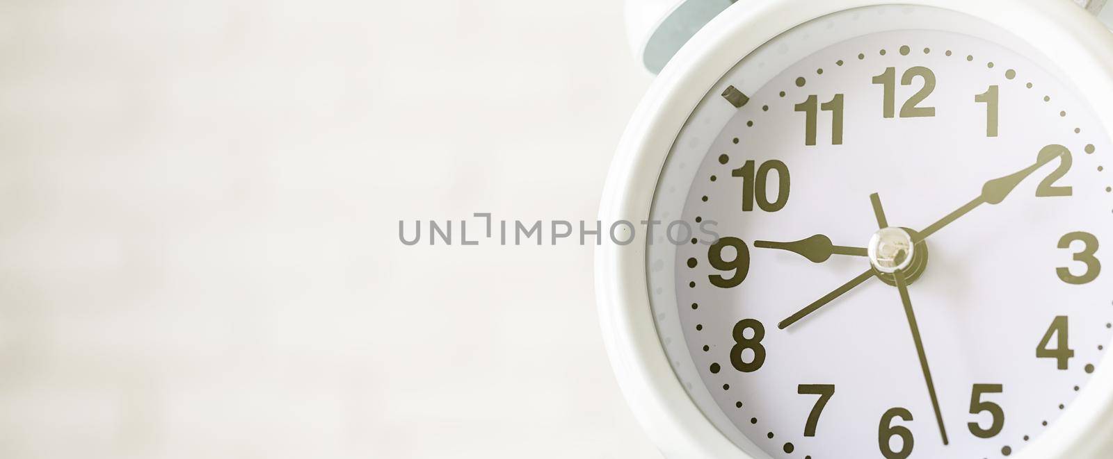 Time management, punctuality, business metaphors. Close up of white vintage alarm clock with hands on nine ten on white brick wall background with copy space