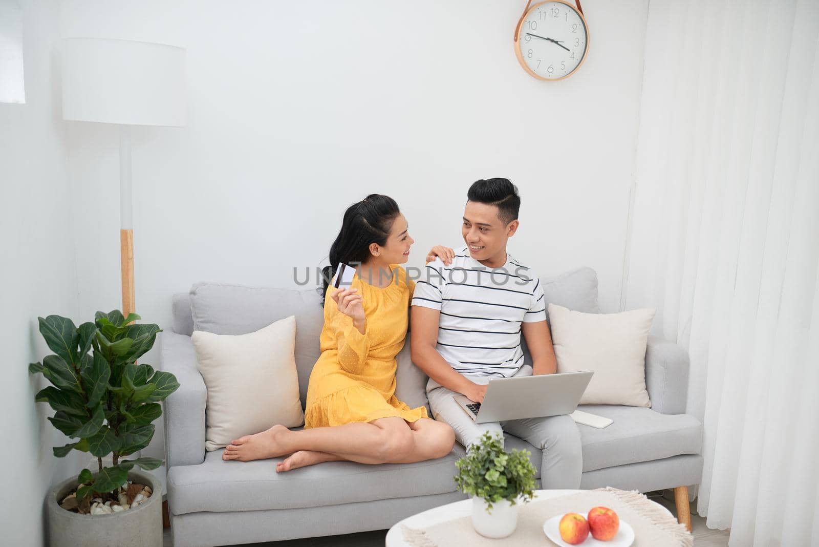 Choosing what to get. Beautiful young woman holding credit card and pointing laptop with smile while sitting together with her husband on the couch