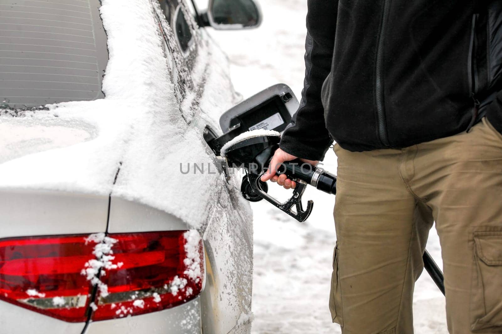 Man filling his snow covered diesel car gas tank at the fuel pump, detail on hand and gasoline nozzle. by Ivanko